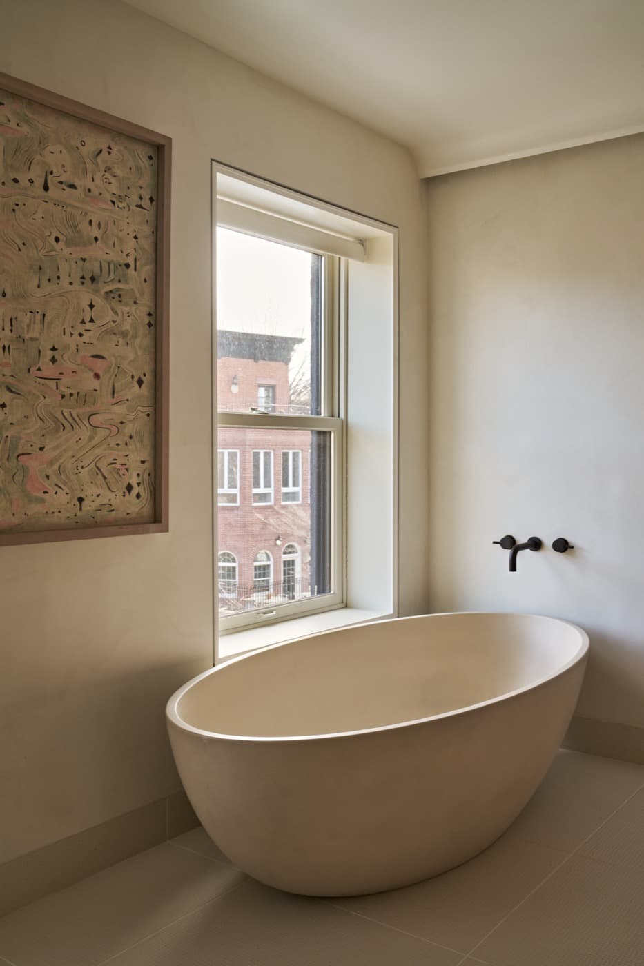 Bathroom with a freestanding oval soaking tub beneath a deep-set window and dark metal fixtures
