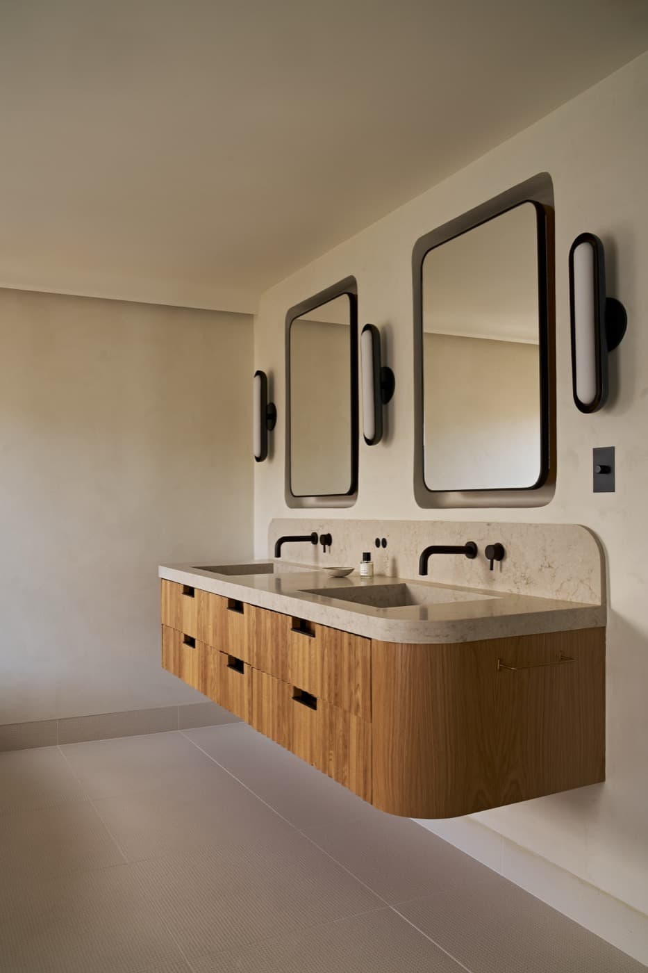 Bathroom featuring a floating timber vanity with curved stone countertop, integrated sinks, and recessed mirrors