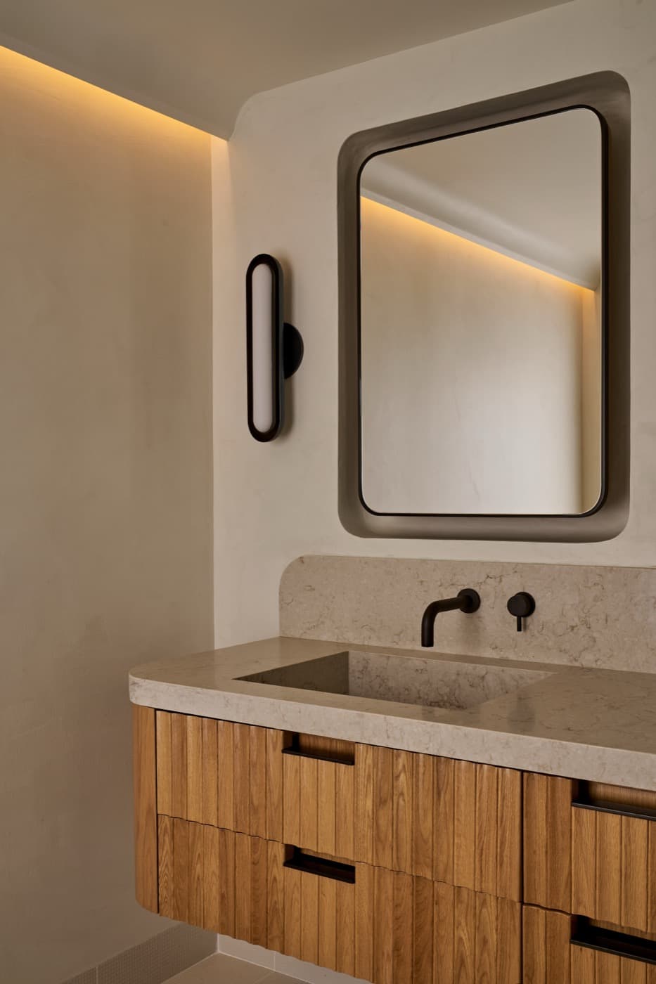 Bathroom vanity with fluted timber cabinetry, integrated pale stone sink, and rounded recessed mirror