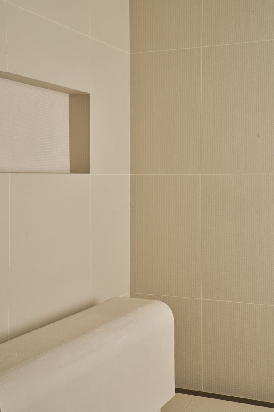 Bathroom shower corner with pale textured tiles, a recessed niche, and curved bench