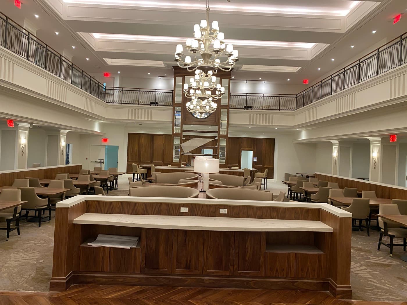 Double-height dining hall with custom timber millwork buffet, pale stone countertop, and grand chandeliers