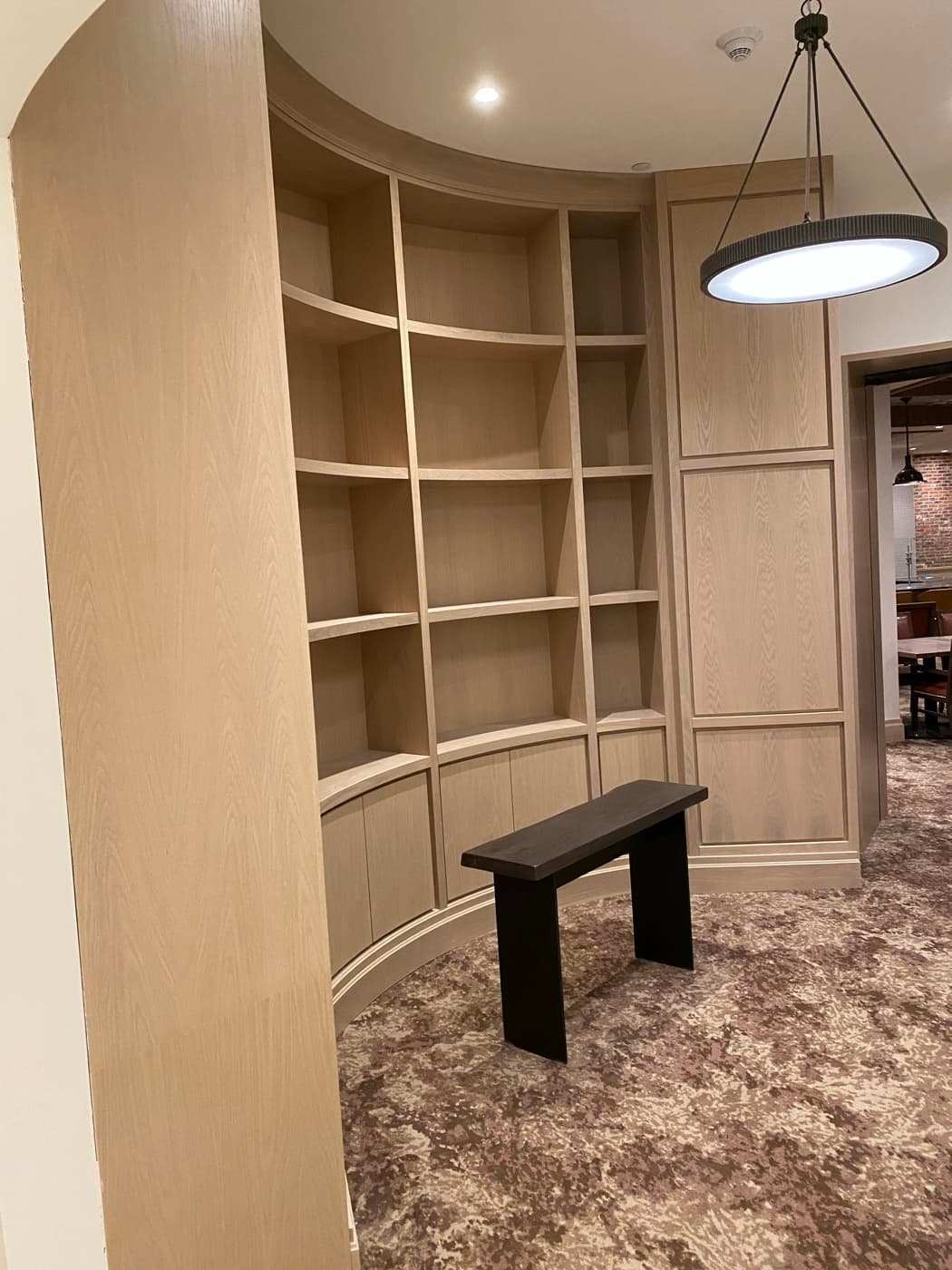 Curved light-toned timber built-in bookcase and matching wall panelling in a carpeted alcove