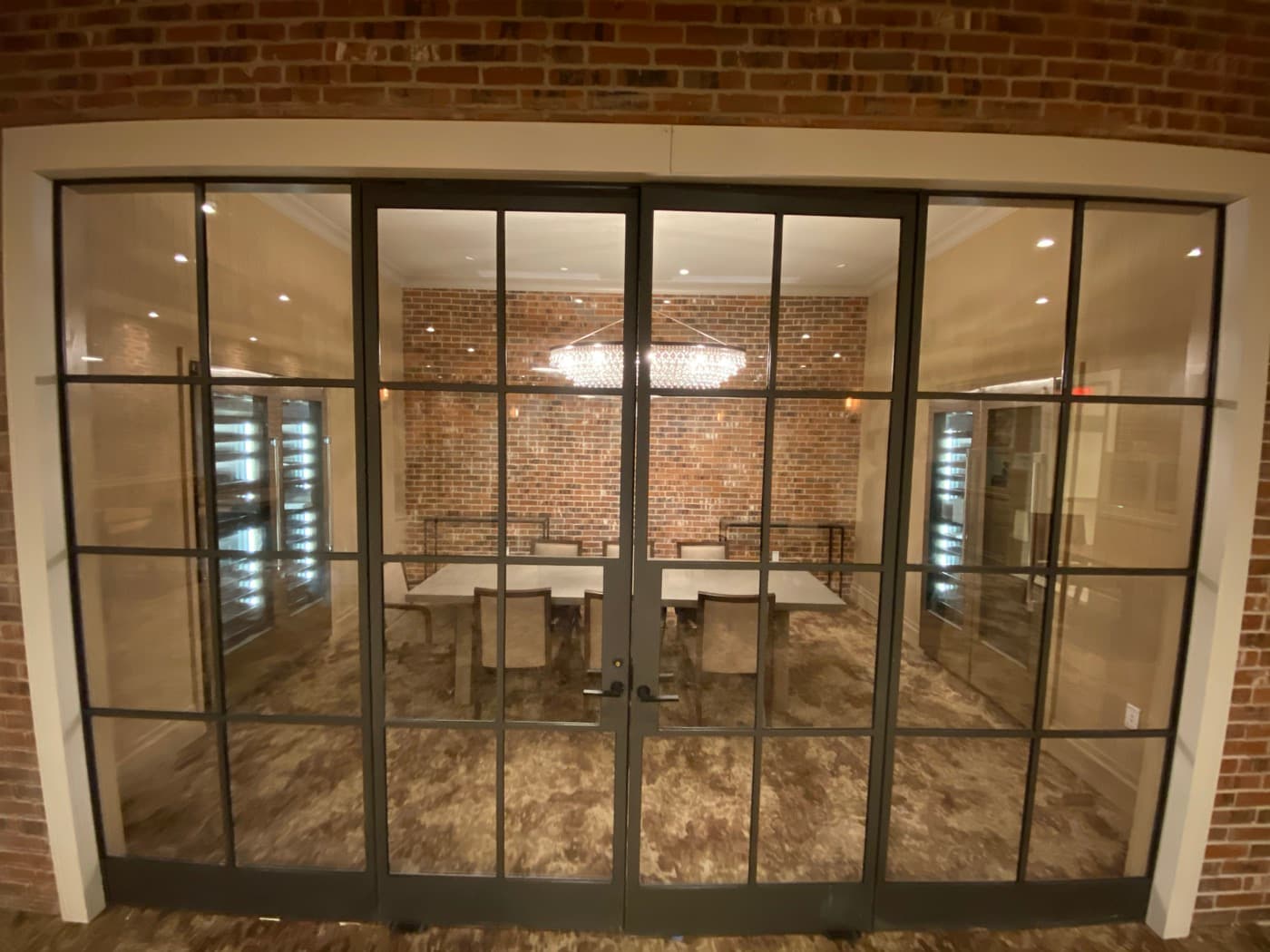 Meeting room viewed through dark metal and glass doors with an exposed brick accent wall