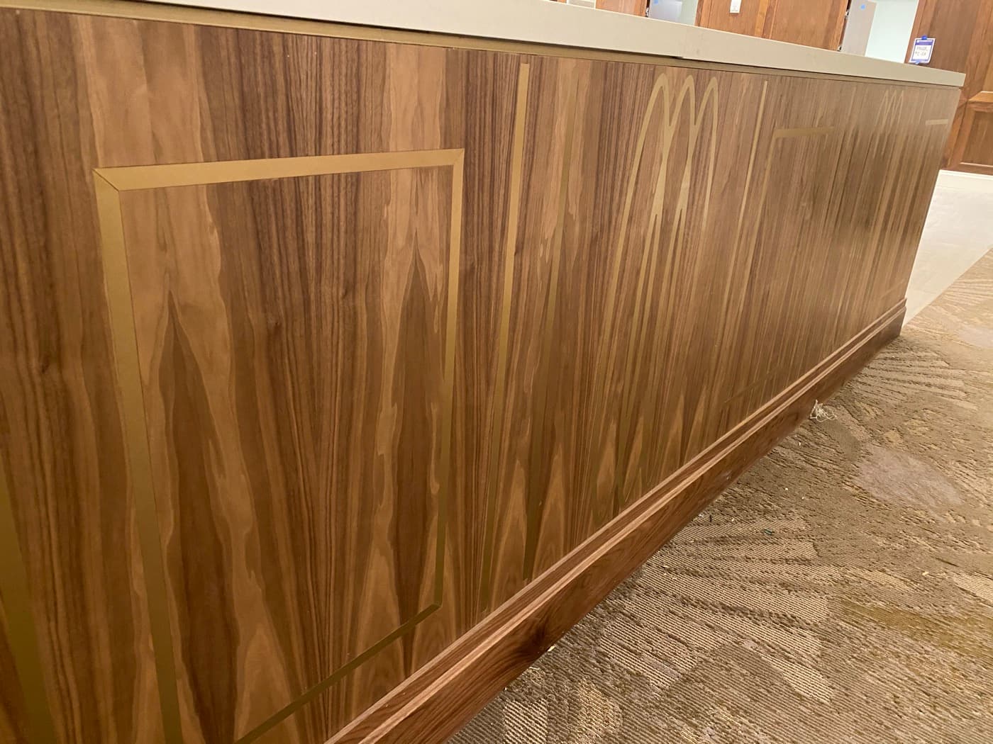 Reception counter featuring warm timber panelling with geometric brass metal inlays and moulded baseboard