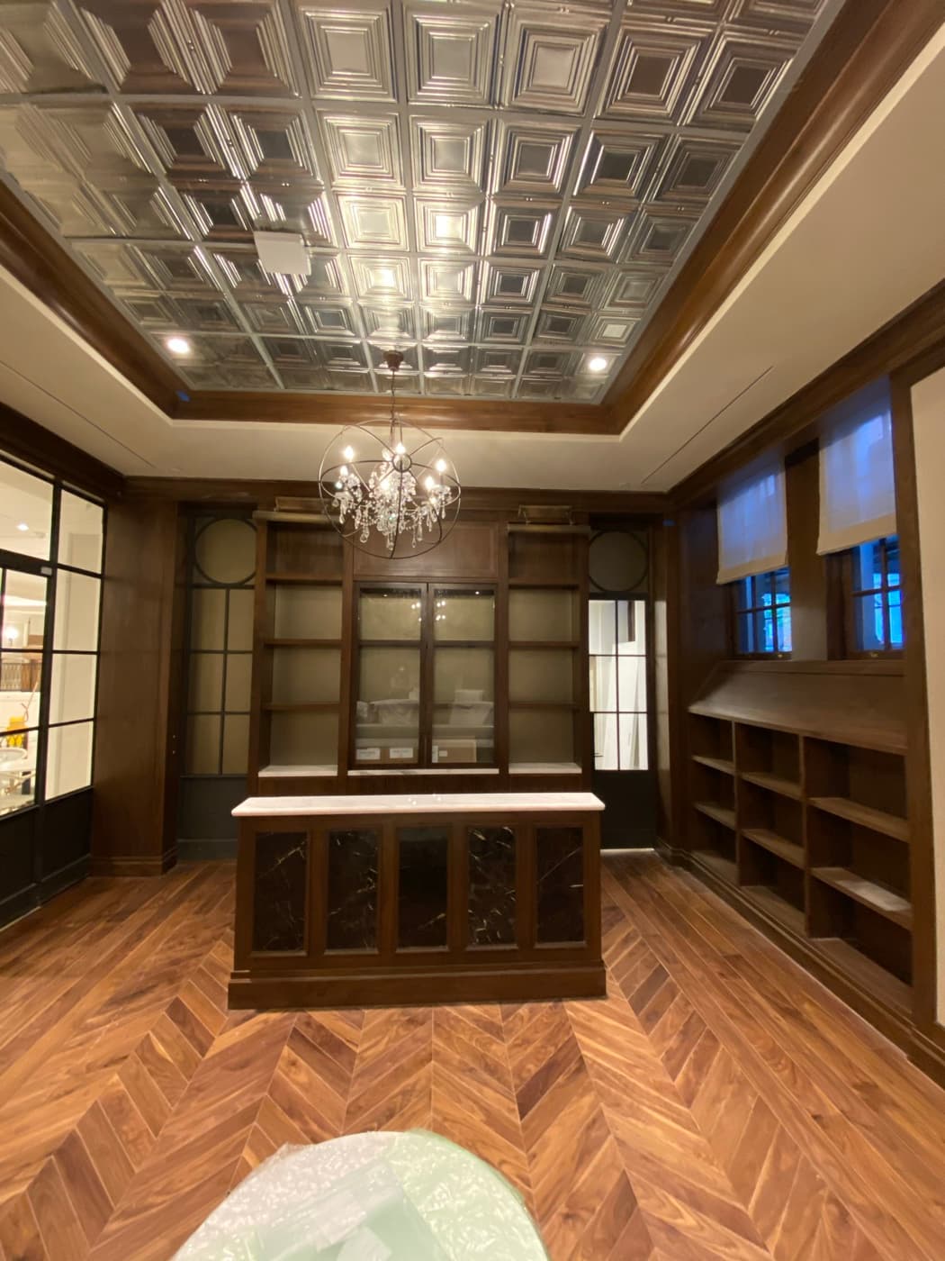 Wood-paneled room with built-in millwork shelving, central island, chevron flooring, and pressed metal ceiling