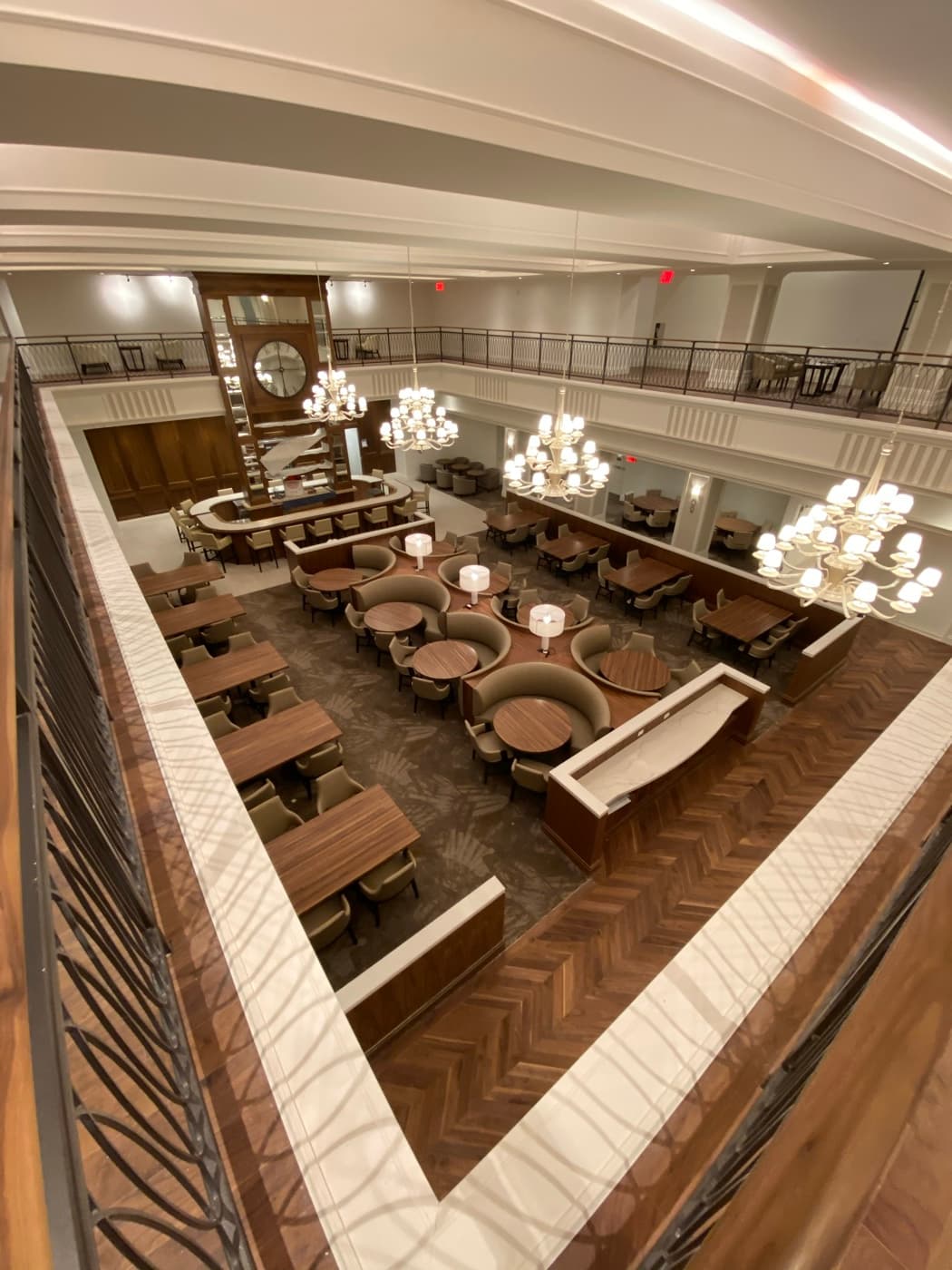 Double-height dining hall with mezzanine balcony, herringbone timber flooring, circular booths, and chandeliers