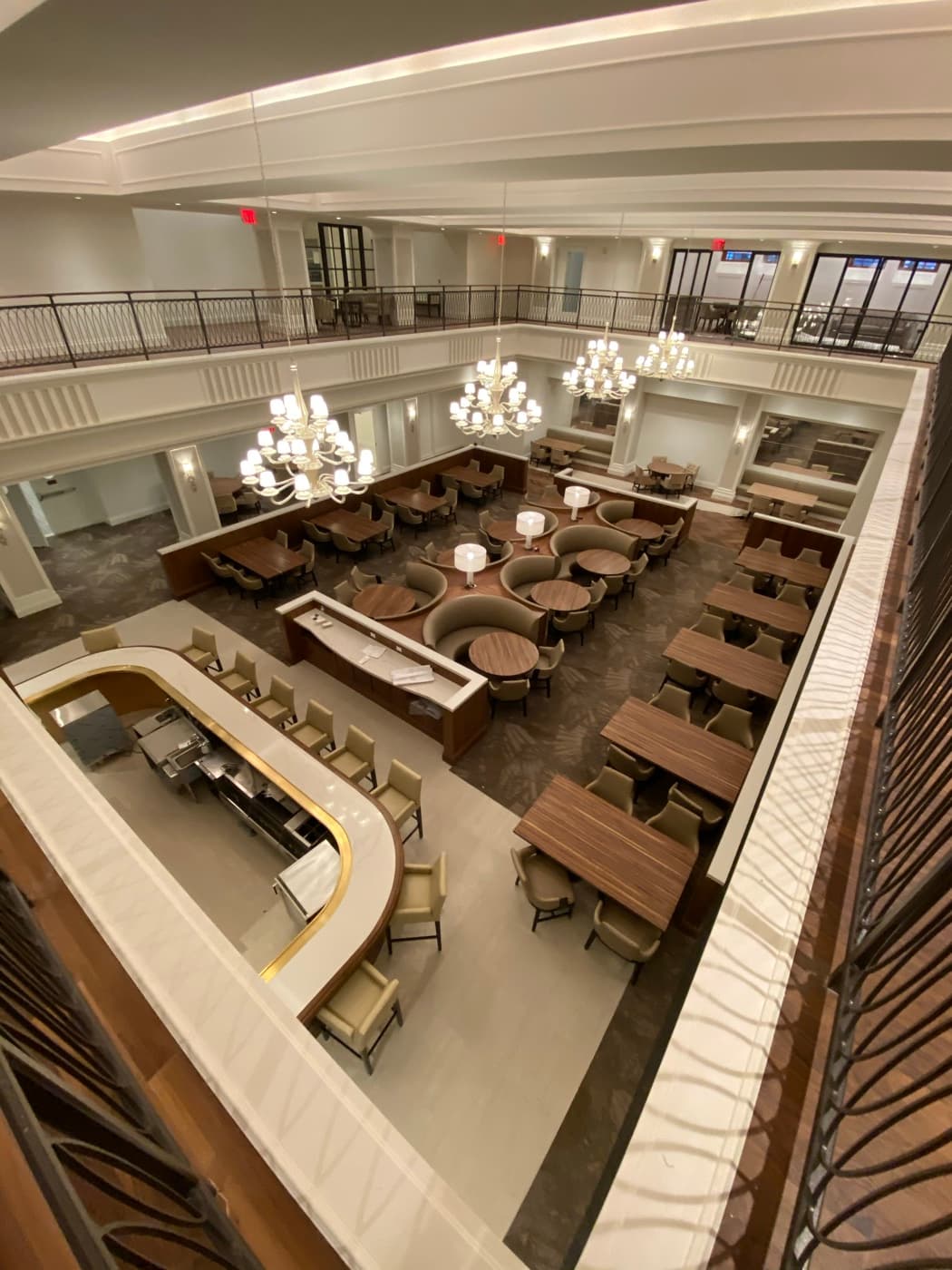 Mezzanine view of a grand dining hall featuring a curved bar, banquette seating, and chandeliers