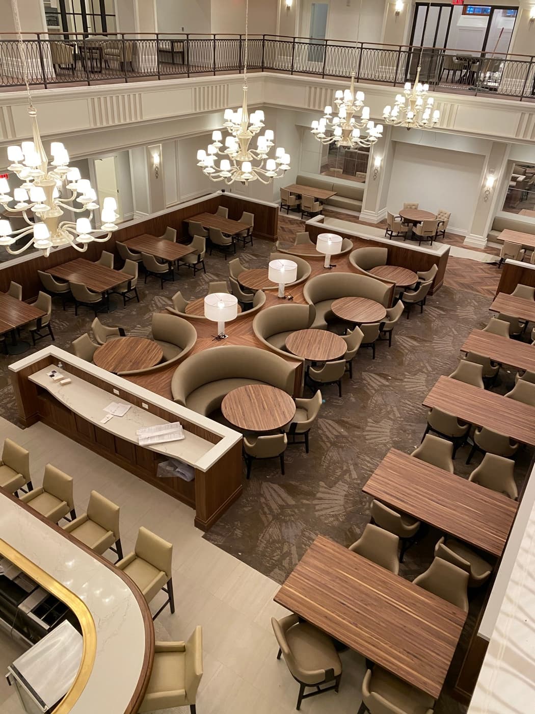 Double-height dining hall with custom curved timber banquettes, matching tables, and stone-topped millwork counters