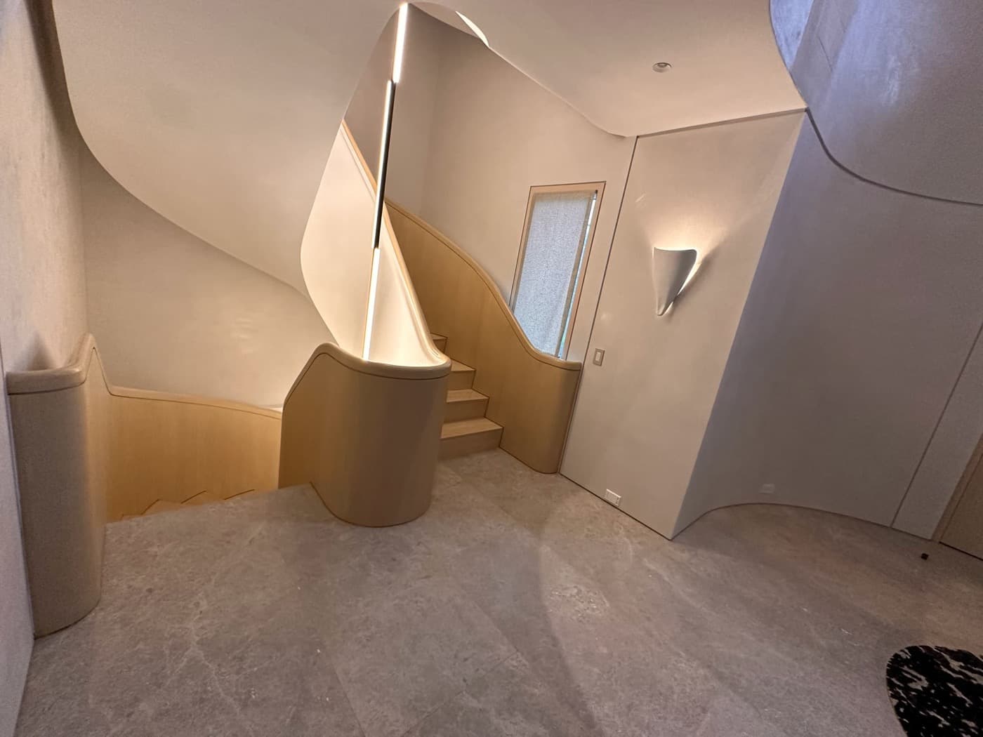 Sculptural stair landing featuring custom curved timber balustrades, integrated lighting, and pale stone flooring