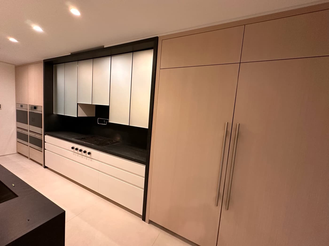 Modern kitchen featuring full-height light timber millwork and a recessed black-framed cooking alcove