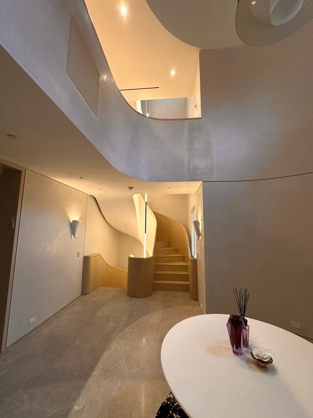 Double-height foyer with a sculptural timber staircase, curved plaster walls and stone flooring