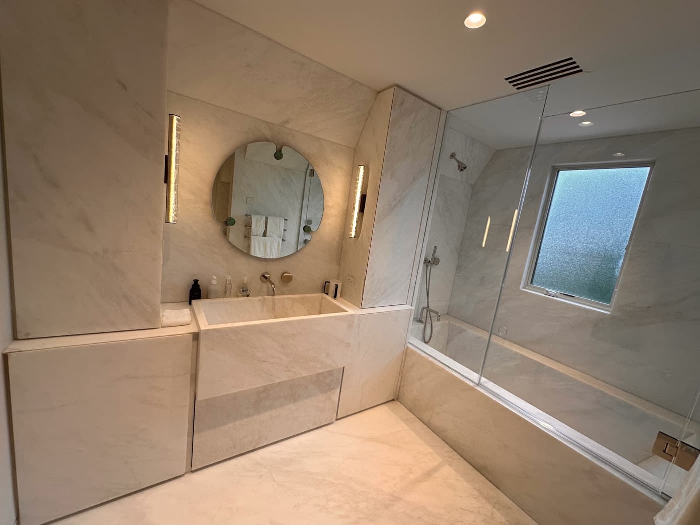 Bathroom with custom pale veined stone vanity, integrated sink, matching cabinetry, and bathtub