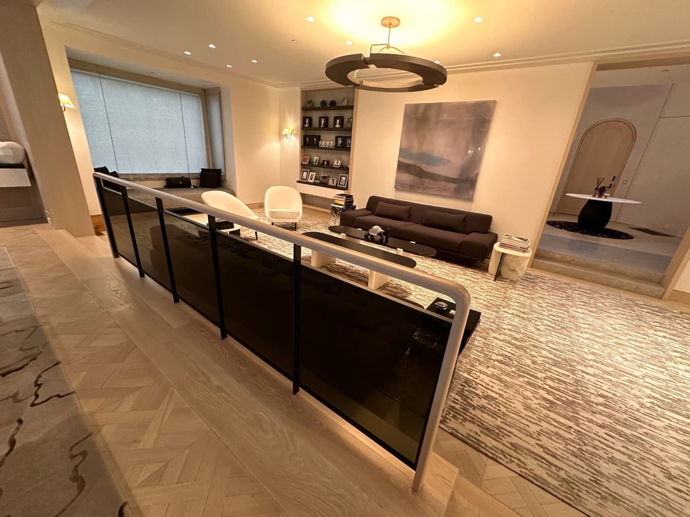 Living room with dark tinted glass railing, pale herringbone timber flooring, and built-in shelving