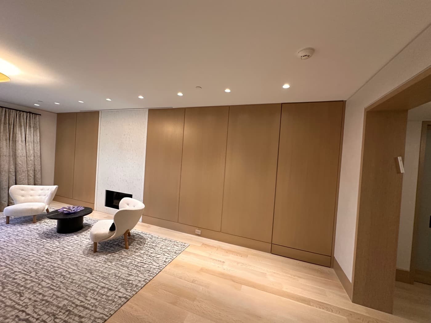 Living room with full-height light timber wall panelling and a pale stone fireplace surround