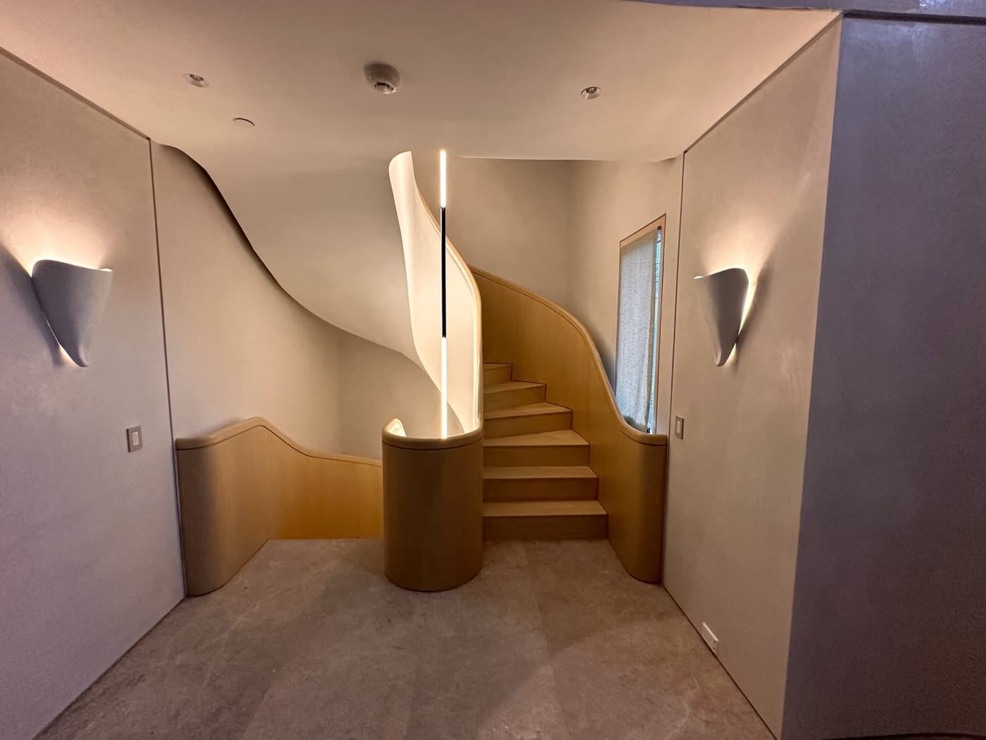 Foyer with a sweeping curved timber staircase, solid wood balustrade, and modern wall sconces
