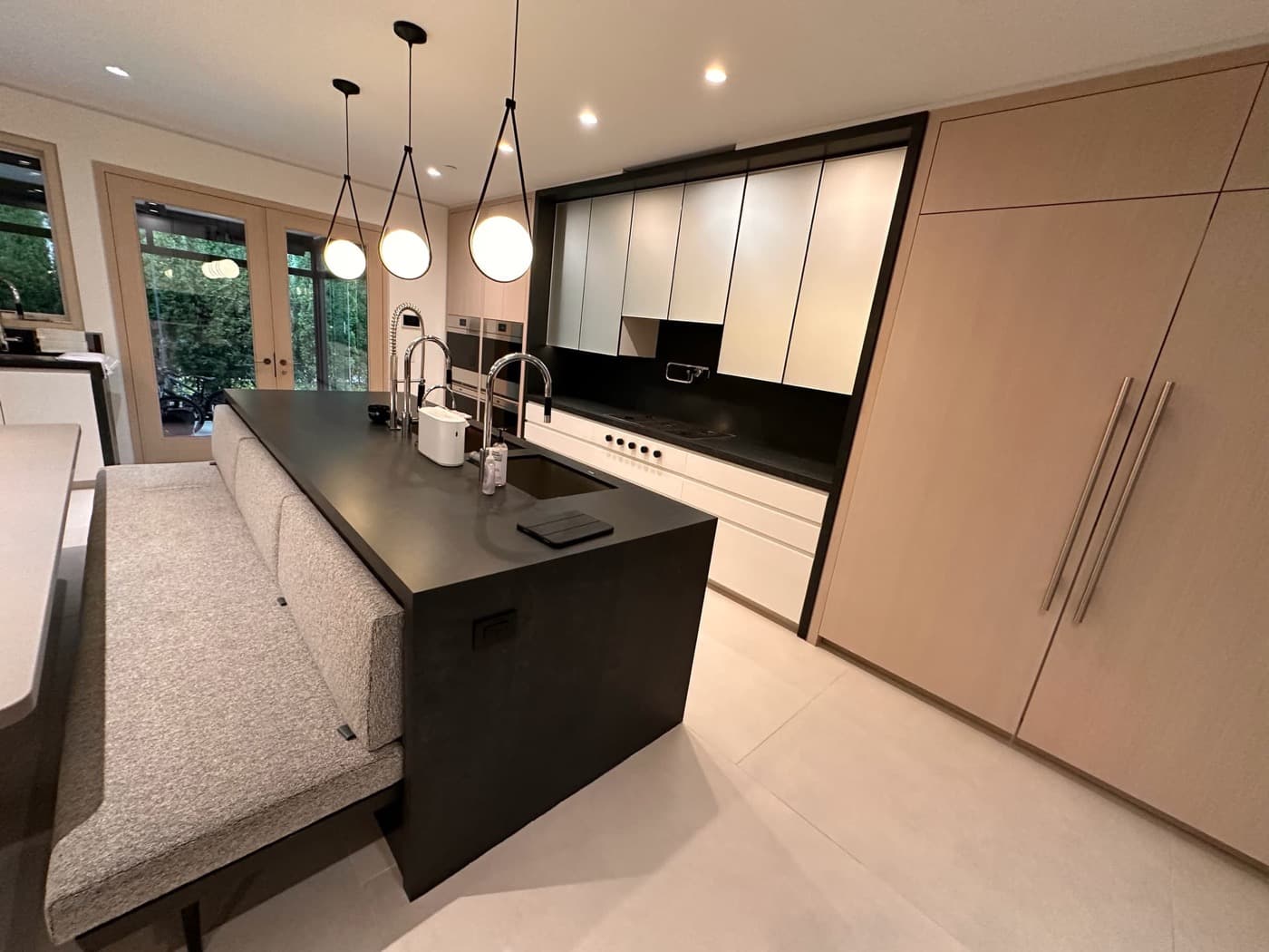 Modern kitchen with a dark waterfall island, integrated banquette seating, and light timber cabinetry