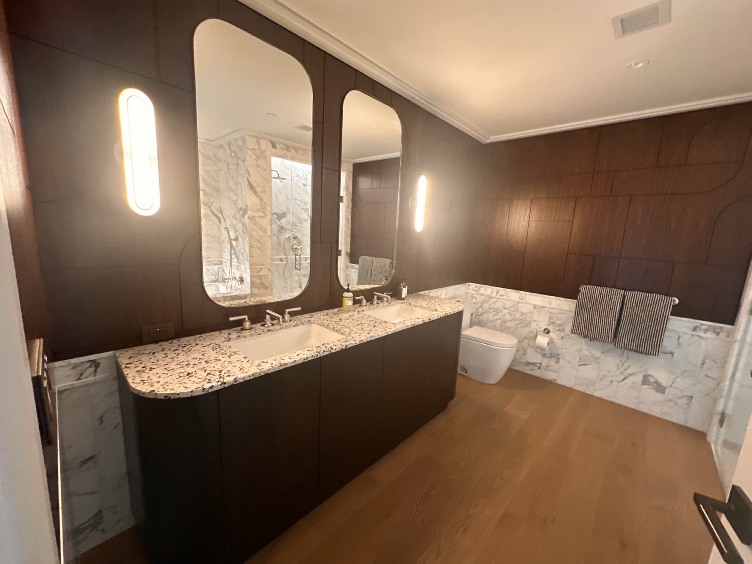 Bathroom with dark timber wall panelling, pill-shaped mirrors, and speckled stone double vanity