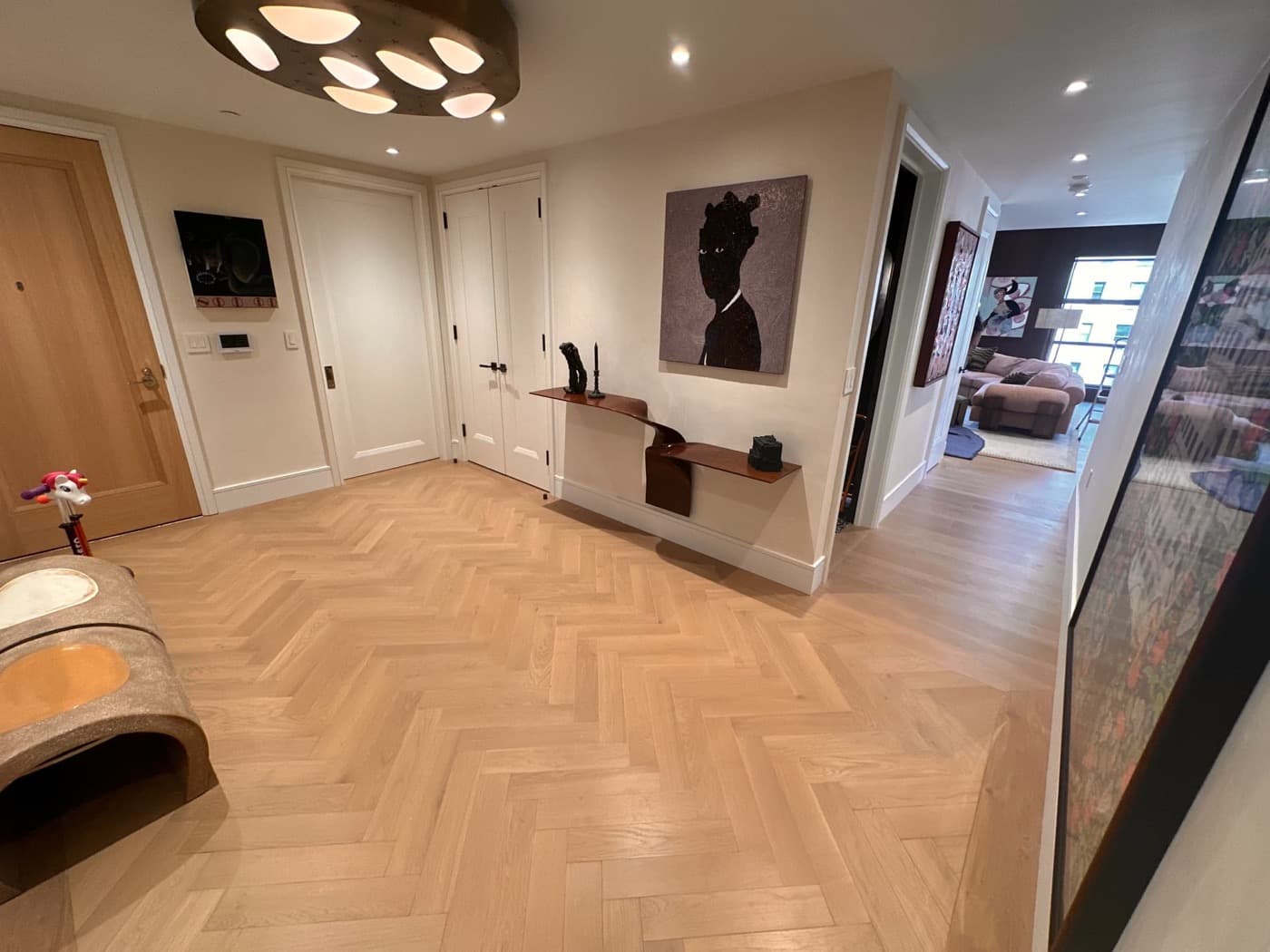 Apartment foyer featuring light timber herringbone flooring, custom white doors, and a sculptural ceiling fixture