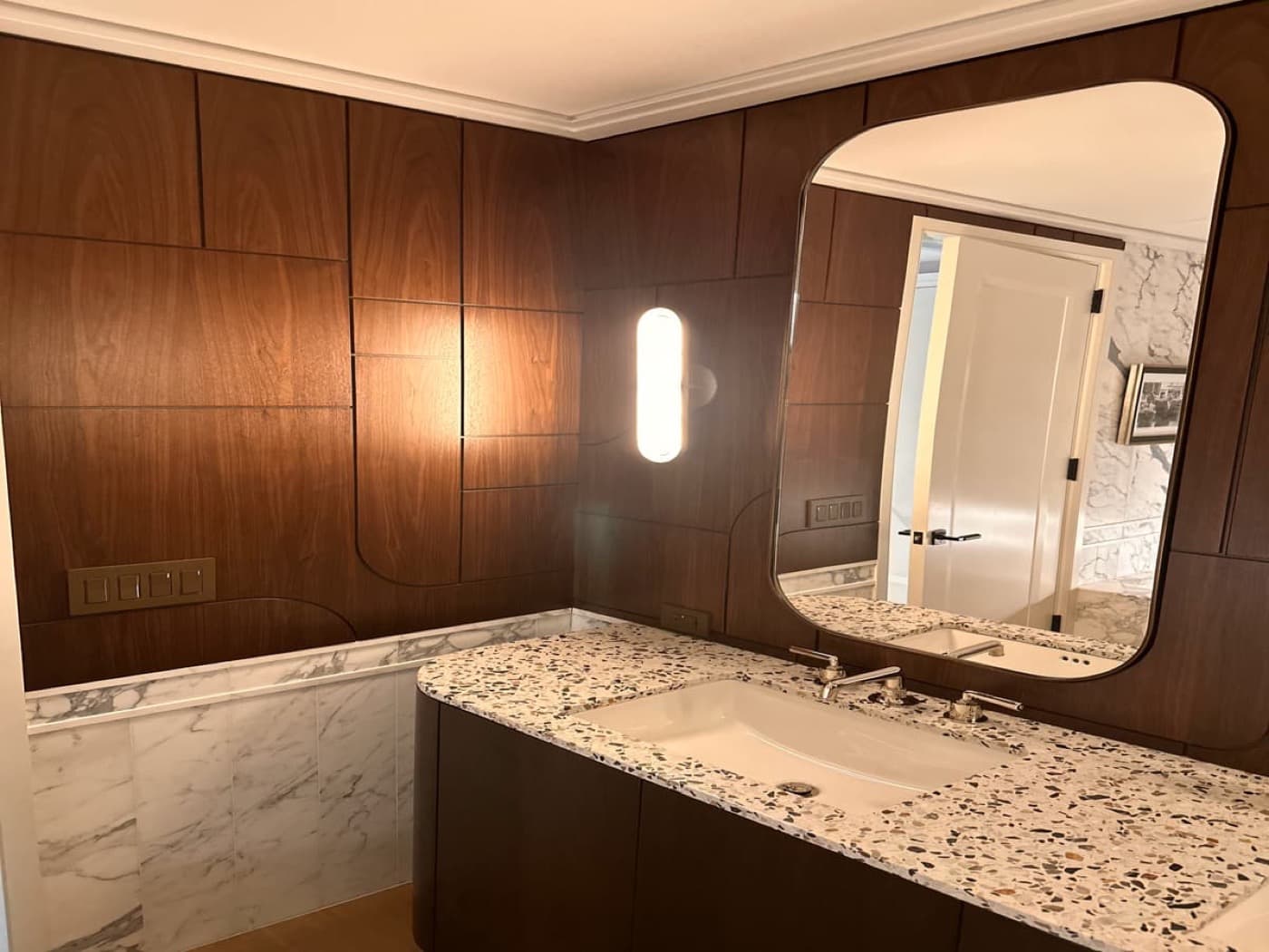 Bathroom with custom warm wood wall panelling, integrated curved mirror and speckled stone vanity