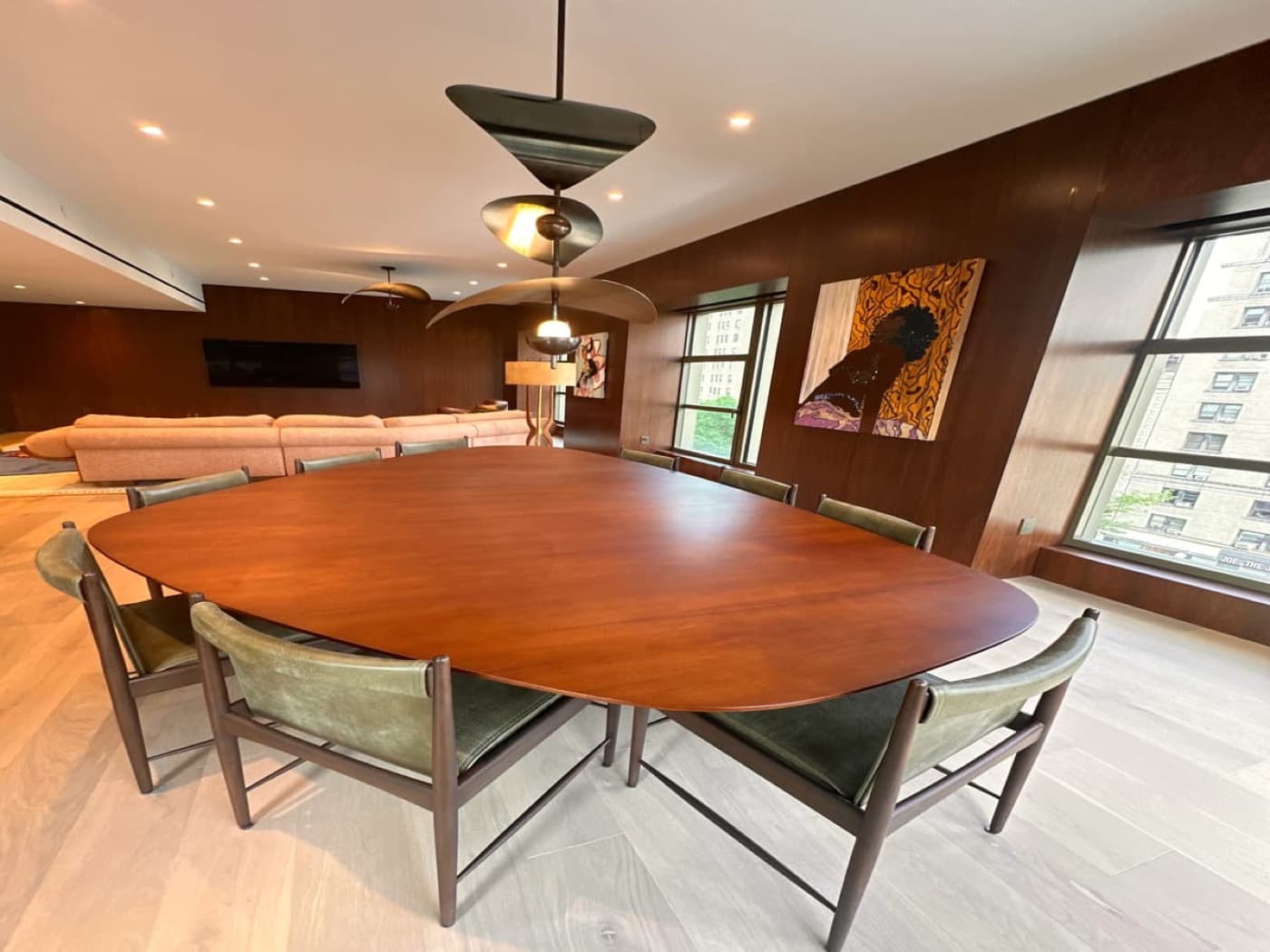Dining room featuring dark timber wall panelling, large timber table, and sculptural pendant lighting