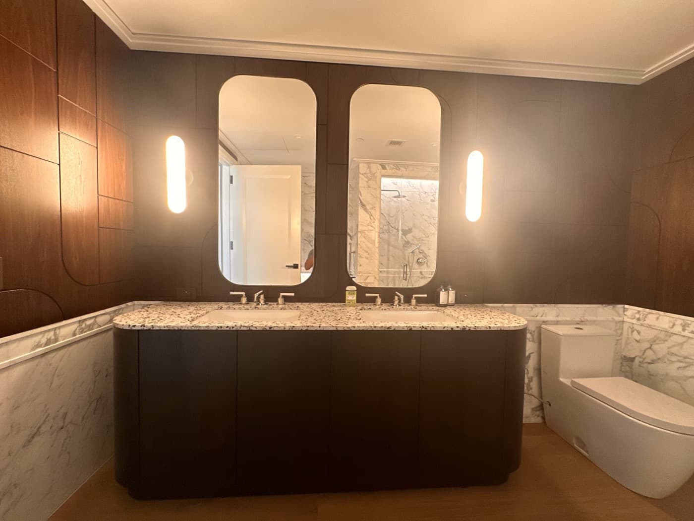 Bathroom with dark timber double vanity, speckled stone countertop, matching wood panelling, and arched mirrors