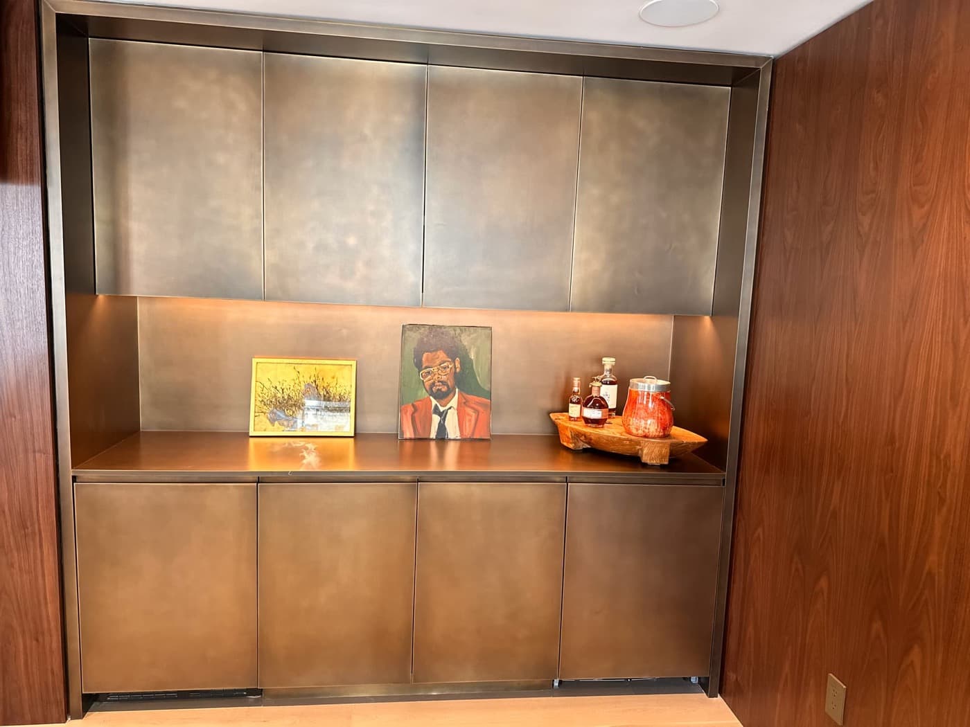 Recessed dry bar with patinated bronze-toned metal cabinetry framed by warm timber wall panelling