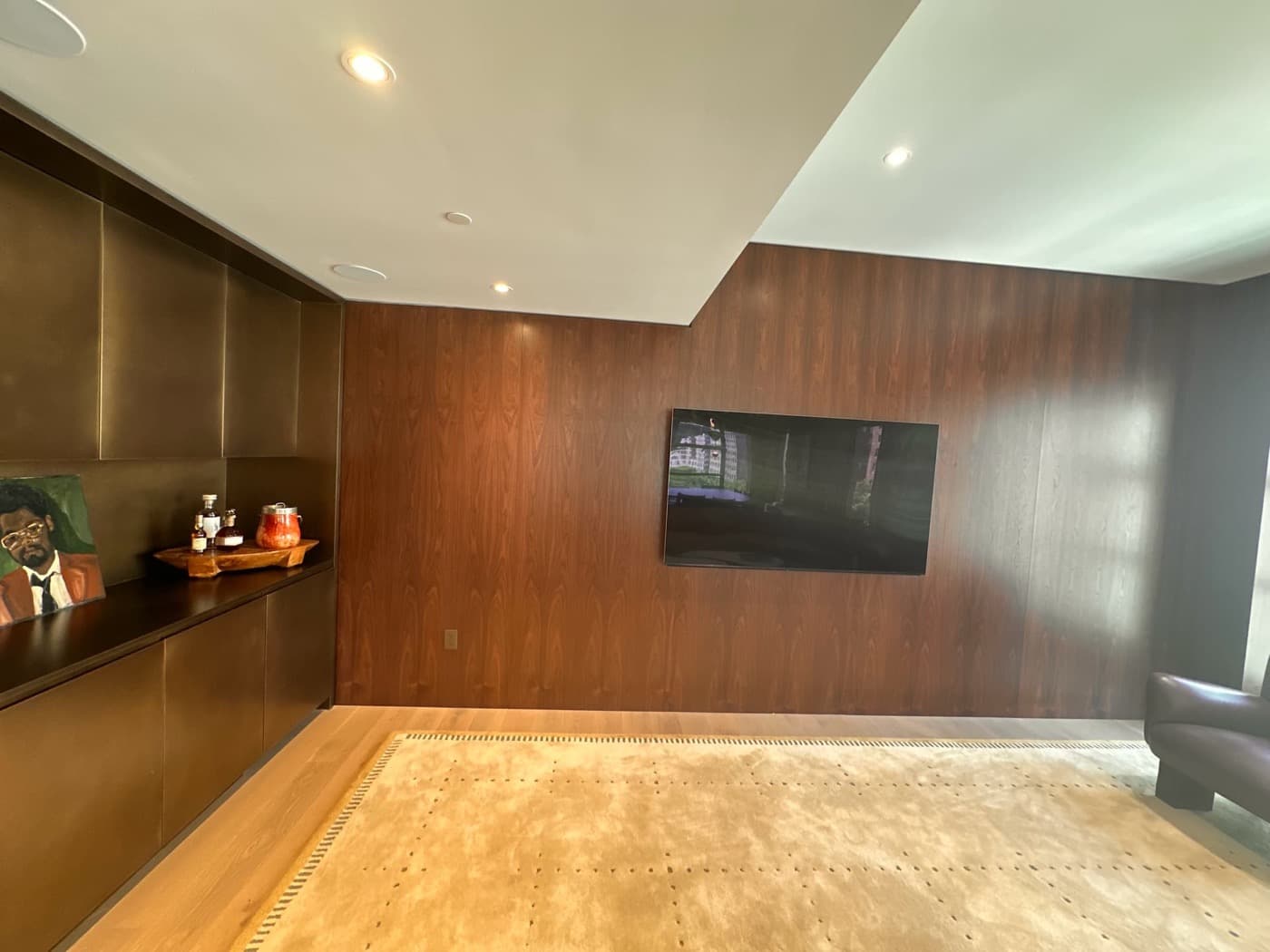 Living area featuring rich wood wall panelling with mounted television beside bronze-toned built-in cabinetry