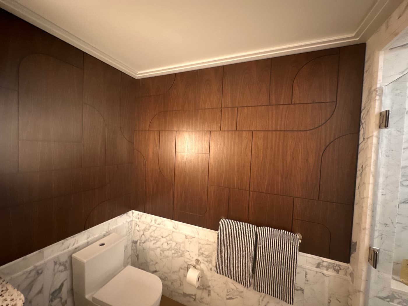 Bathroom with custom patterned dark timber wall panelling above pale veined stone wainscoting