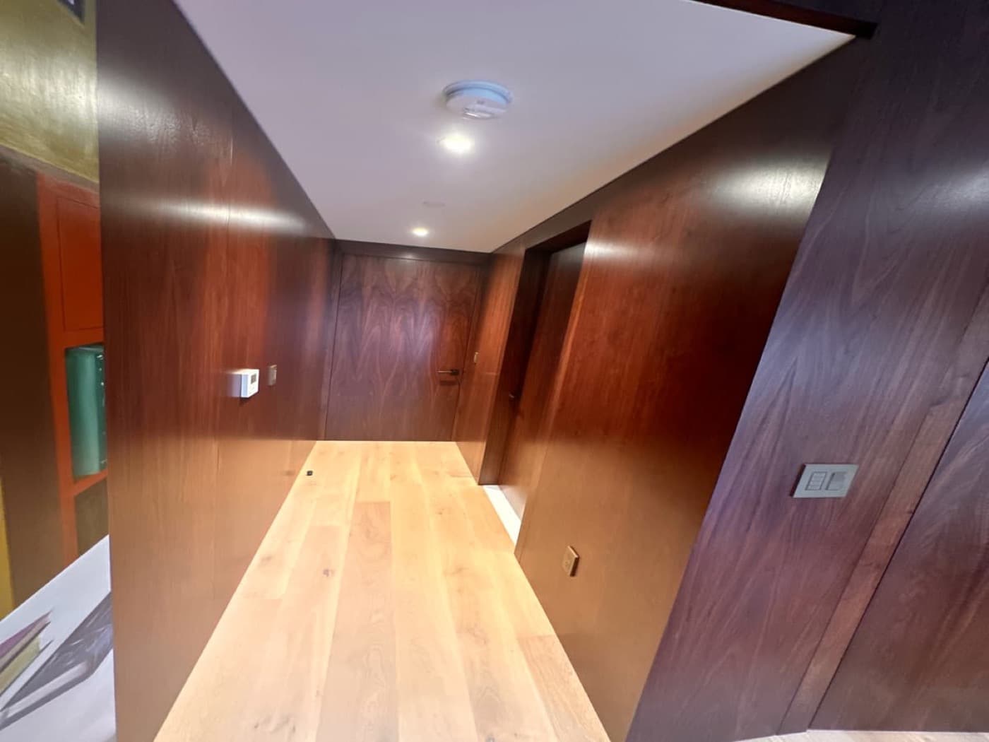 Hallway lined with dark-toned timber wall panelling, seamless flush doors, and light plank flooring