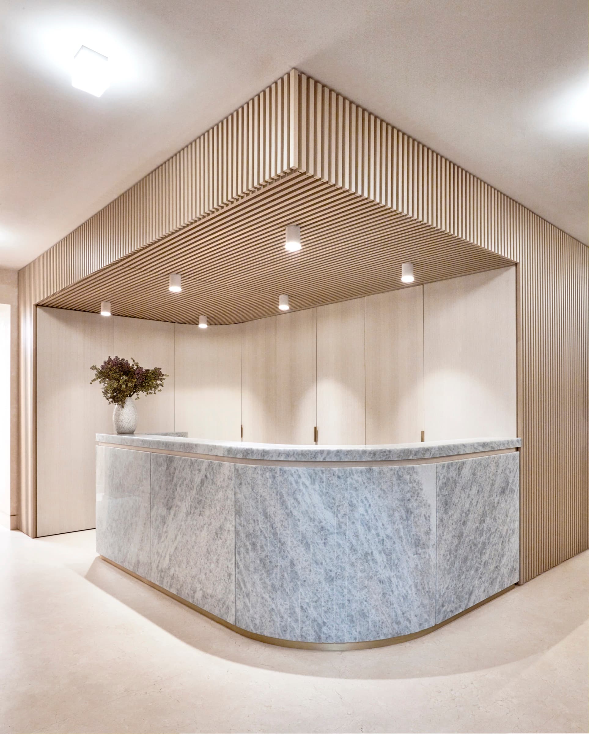 Reception area with curved veined stone desk beneath a light timber slatted canopy
