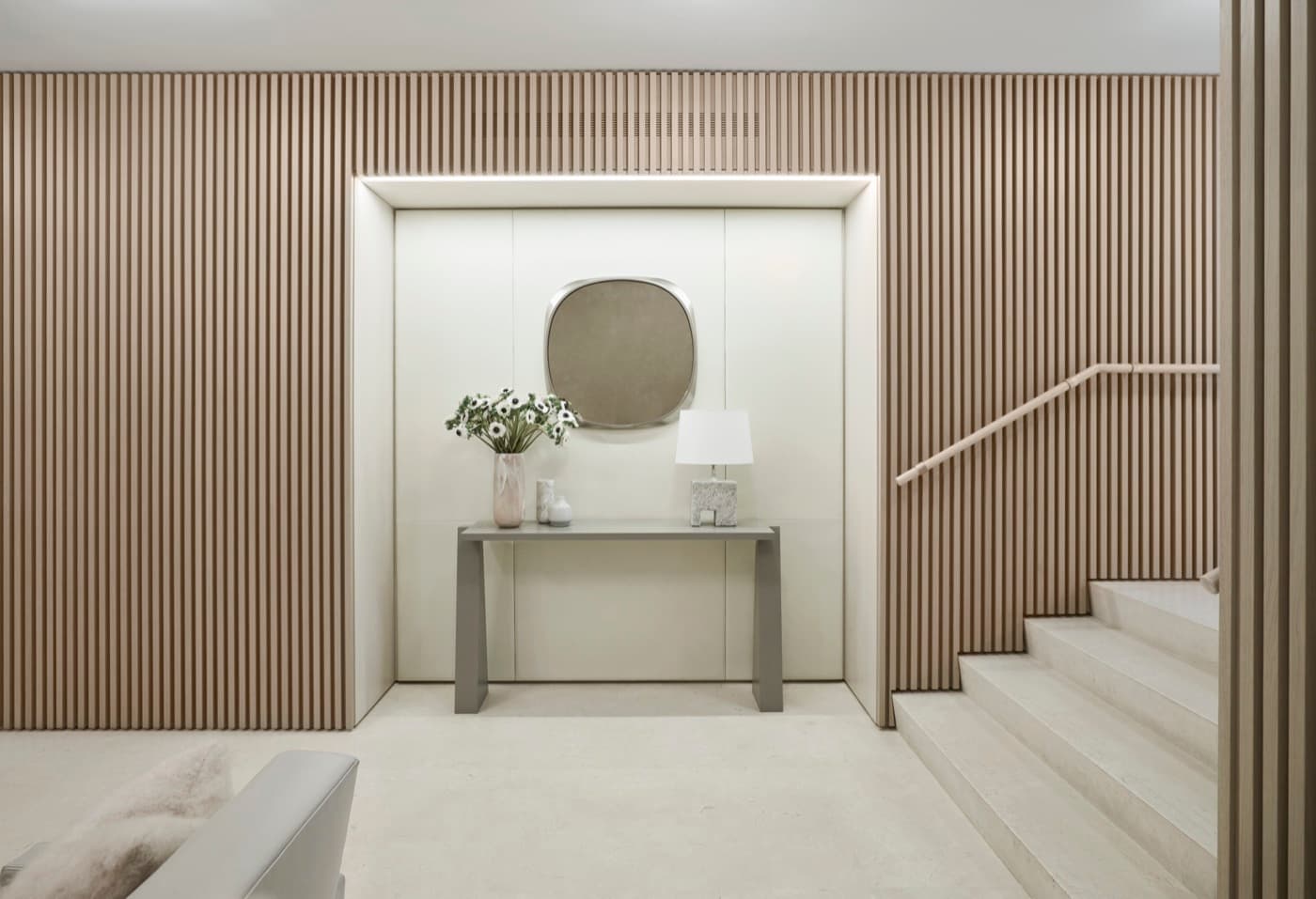 Entryway featuring vertical timber slat wall paneling, illuminated console niche, and pale stone staircase