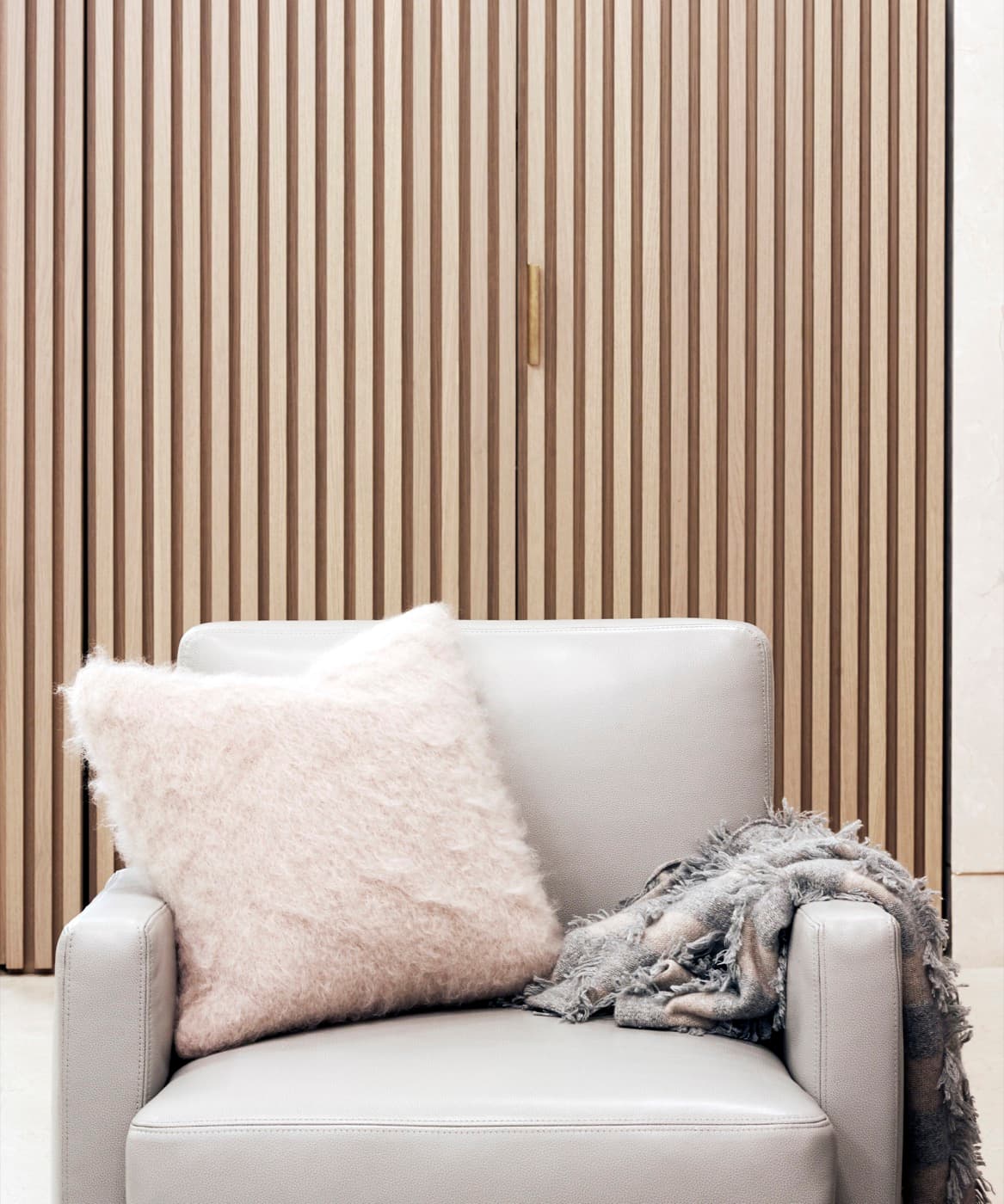 Living room featuring vertical slatted timber millwork doors with a brass-toned pull behind an armchair