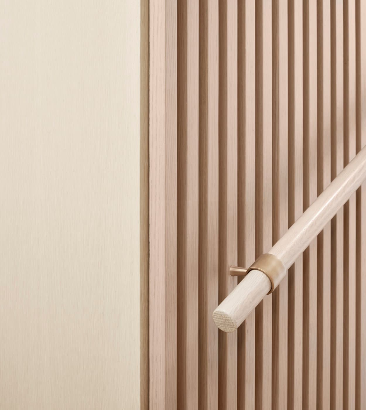 Stairway detail with pale timber slatted wall panelling and round handrail with brass hardware