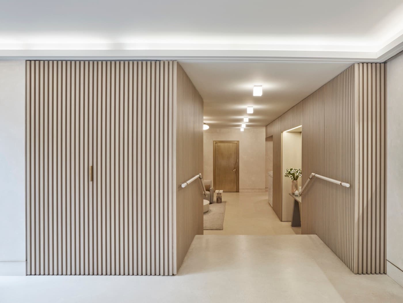 Residential lobby entrance featuring pale timber slatted wall panelling, handrails and light stone flooring