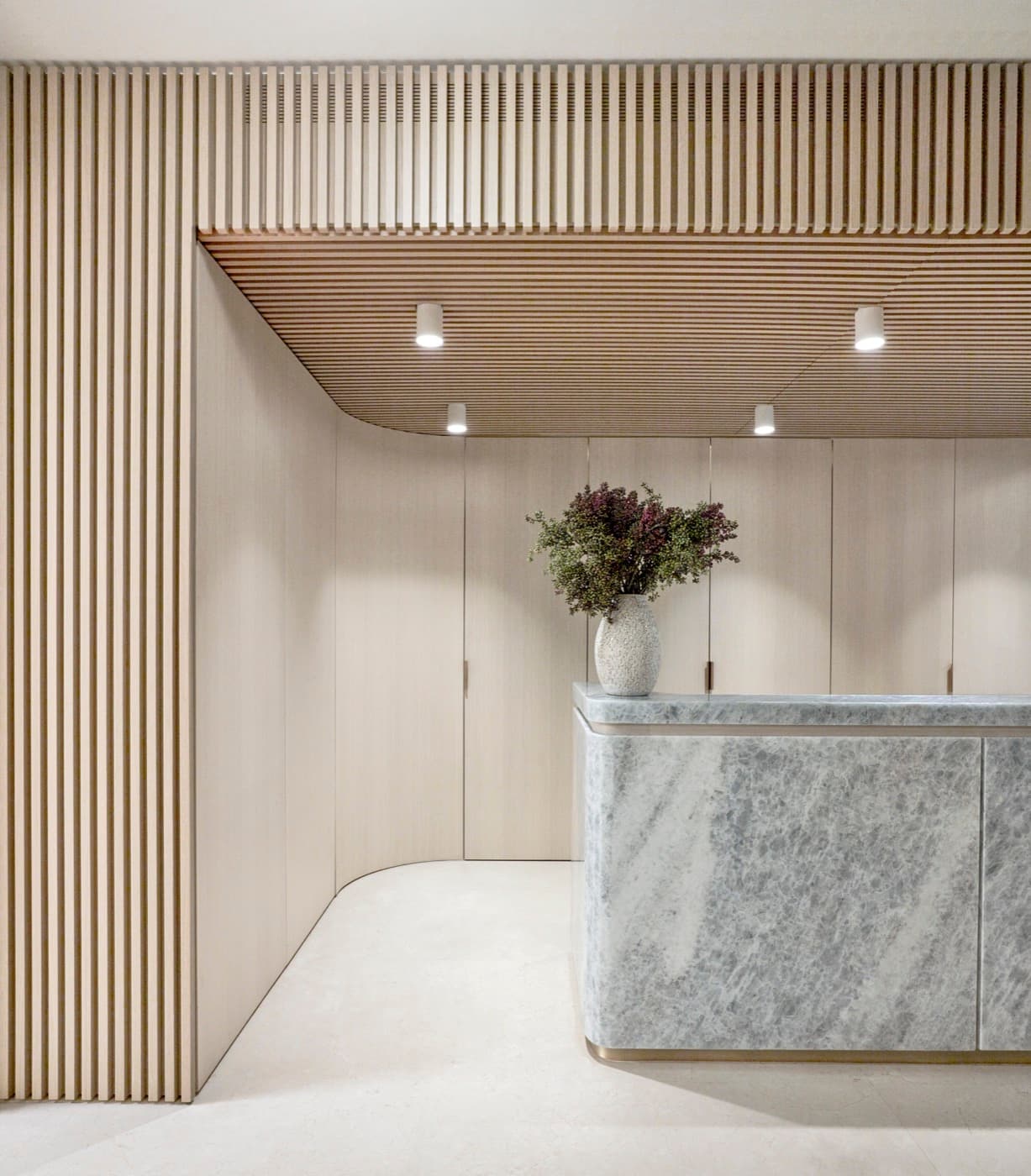 Reception area with timber slatted ceiling, curved wall panelling, and pale veined stone desk