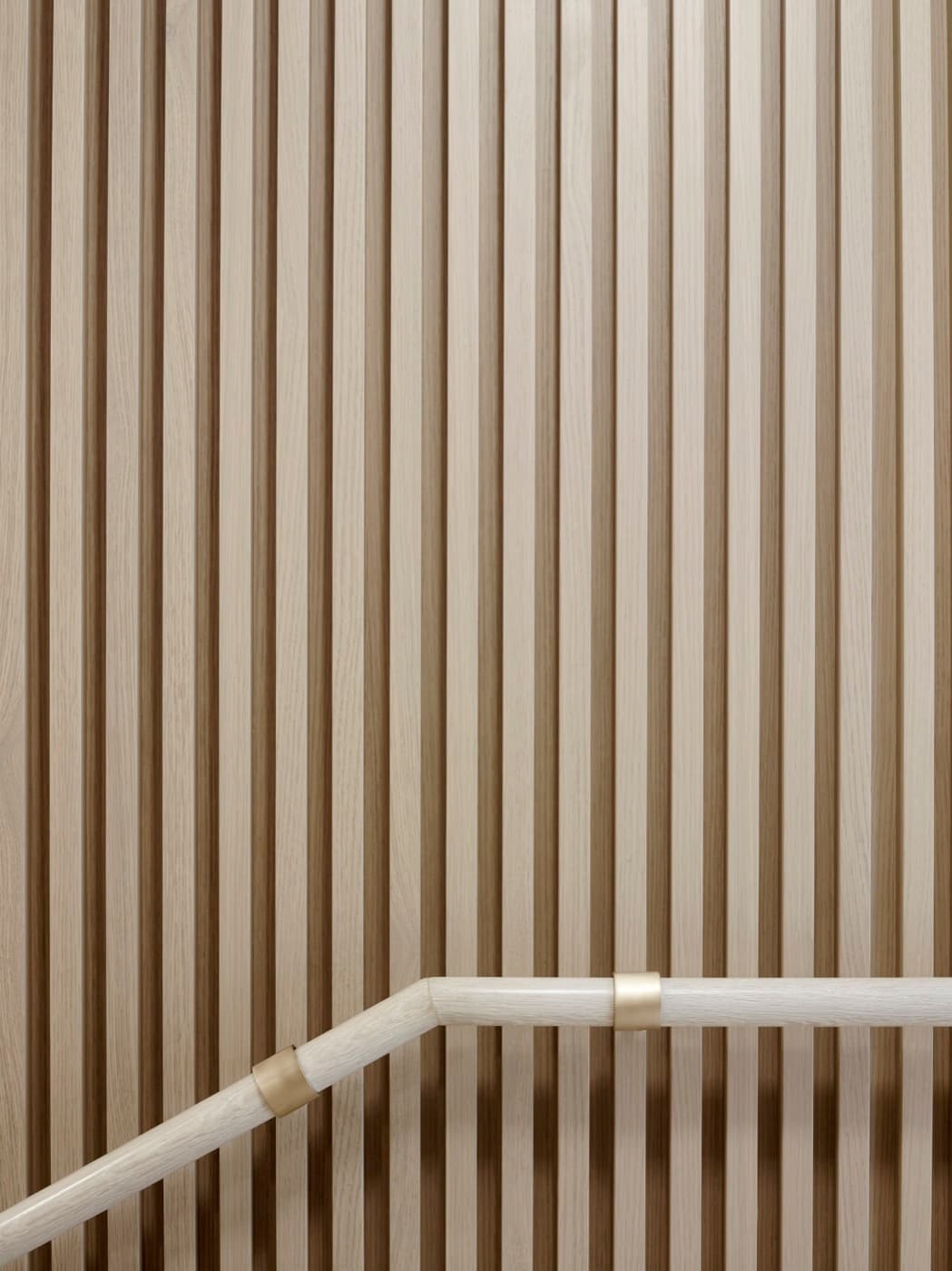 Stairwell wall featuring vertical pale timber slats and a matching handrail with brass fittings