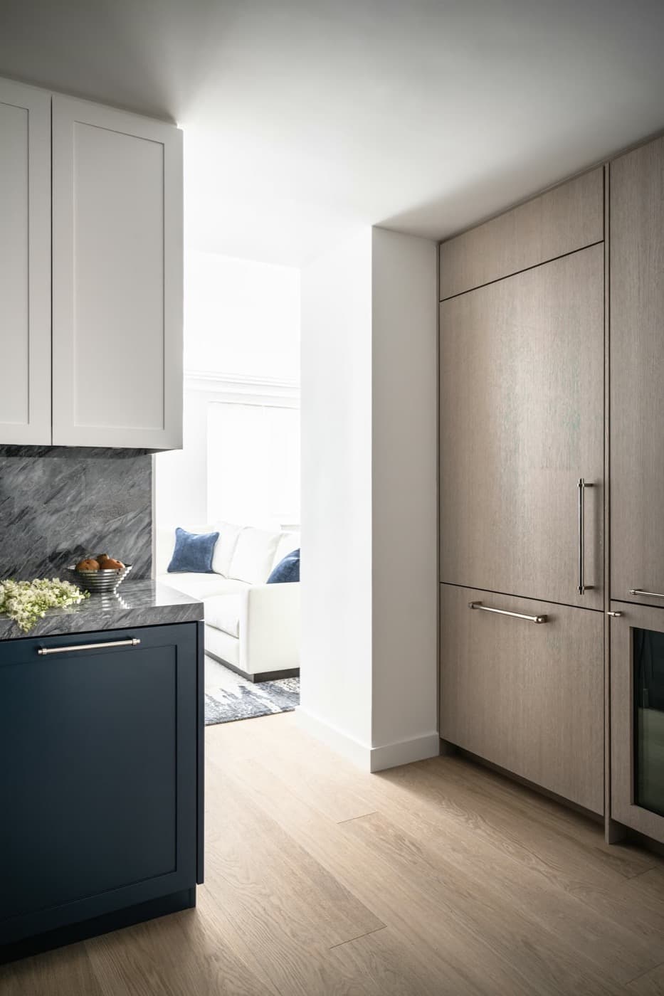 Kitchen featuring tall pale timber-toned cabinetry, dark base millwork, and grey veined stone surfaces