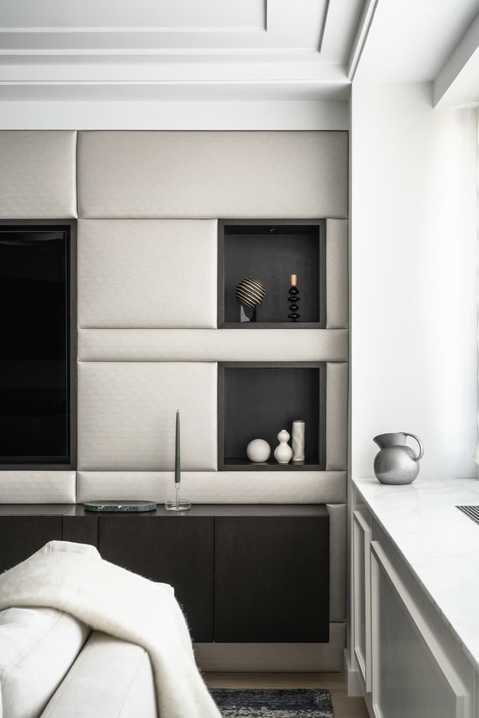 Living room feature wall with upholstered panelling, recessed dark timber display niches, and low cabinetry
