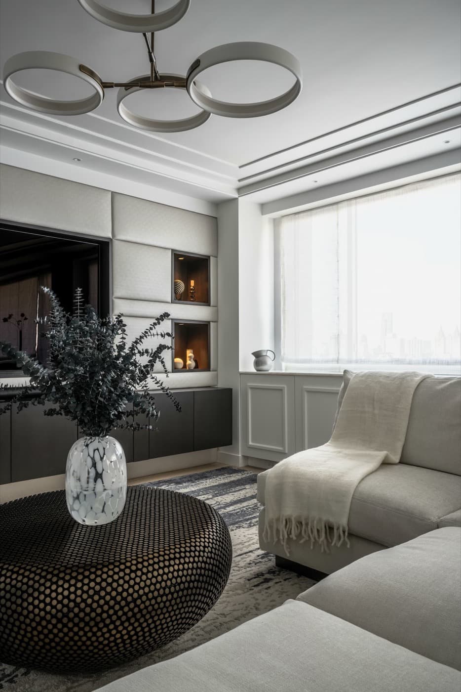 Living room featuring upholstered wall panelling with display niches and a floating dark media console
