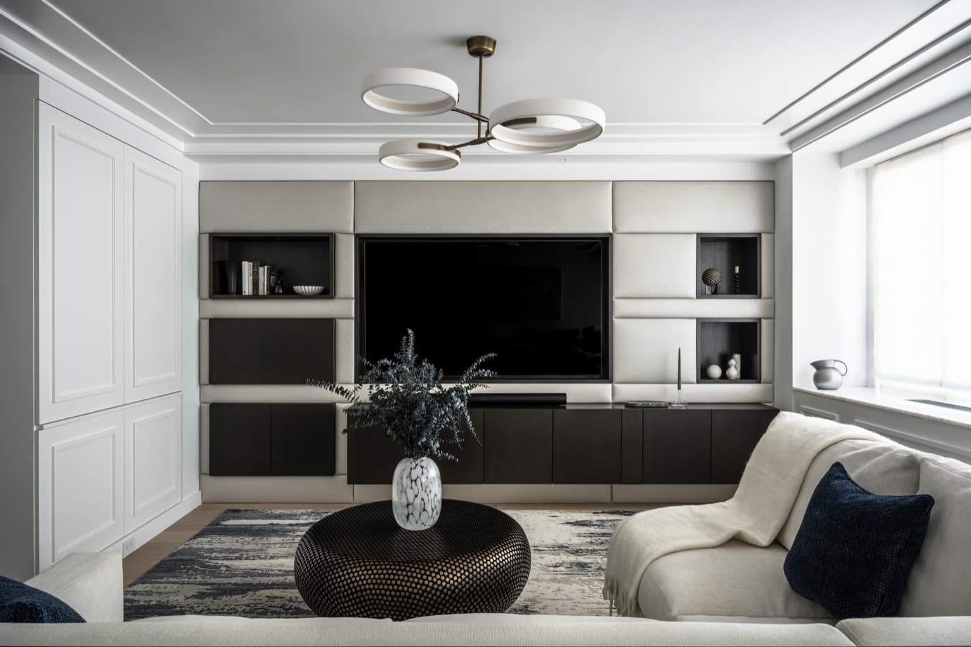 Living room featuring upholstered media wall with integrated dark cabinetry and built-in white millwork
