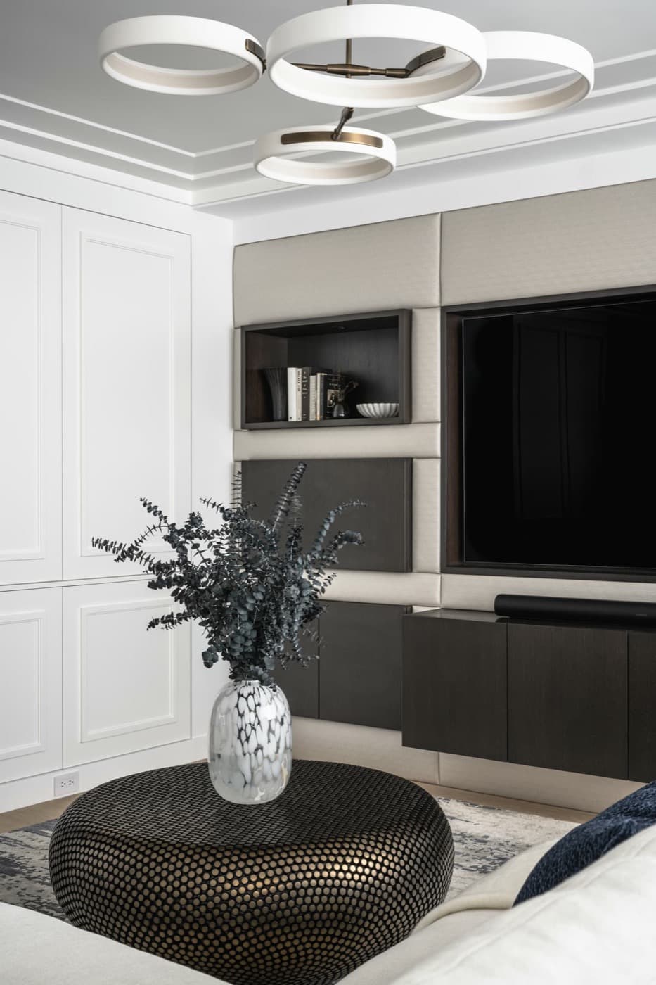 Living room featuring upholstered wall panelling with integrated dark timber media cabinetry and shelving