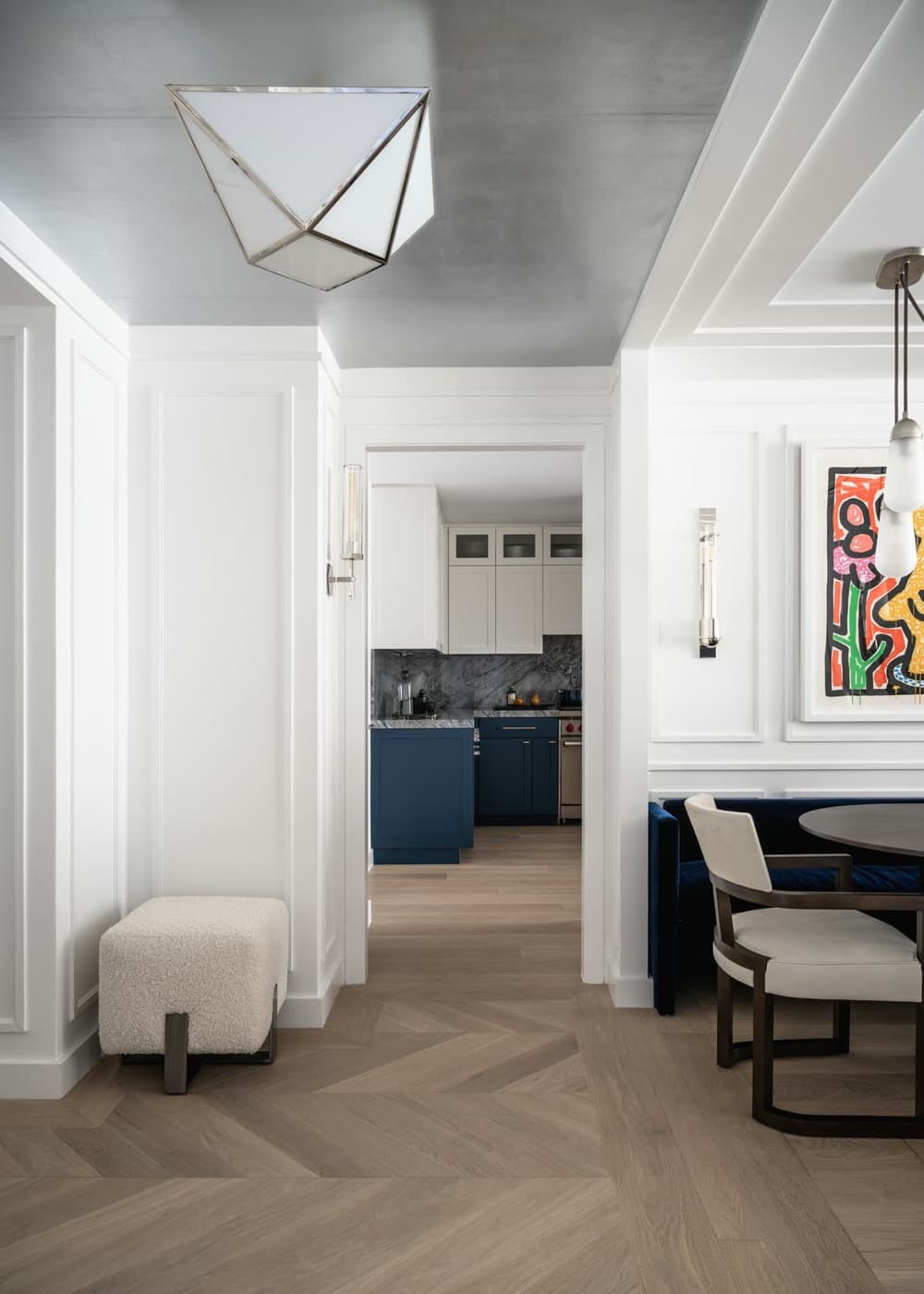 Entryway with white wall panelling and chevron timber flooring looking into a custom kitchen