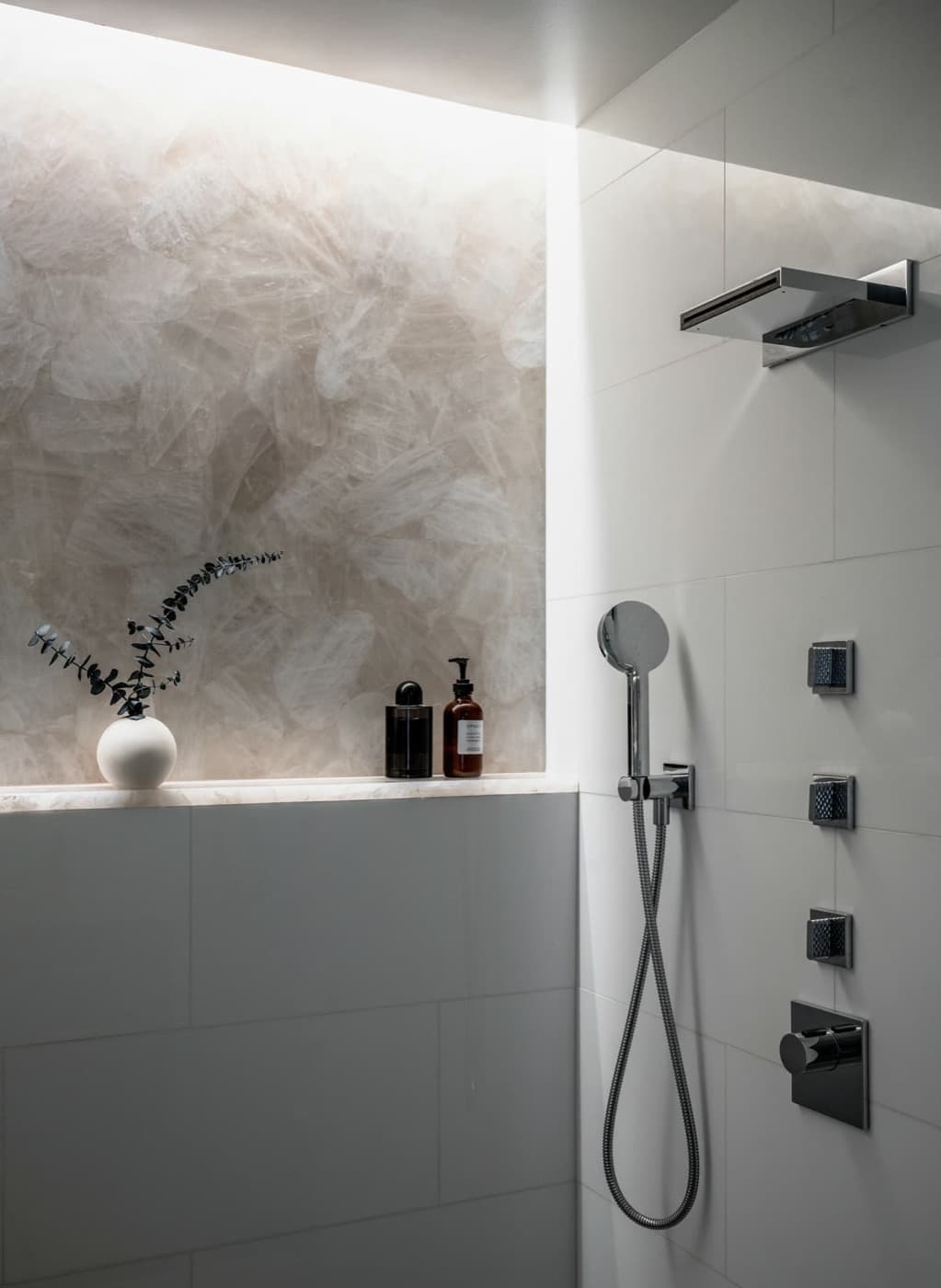 Walk-in shower featuring an illuminated translucent stone wall, white tiling, and chrome fixtures