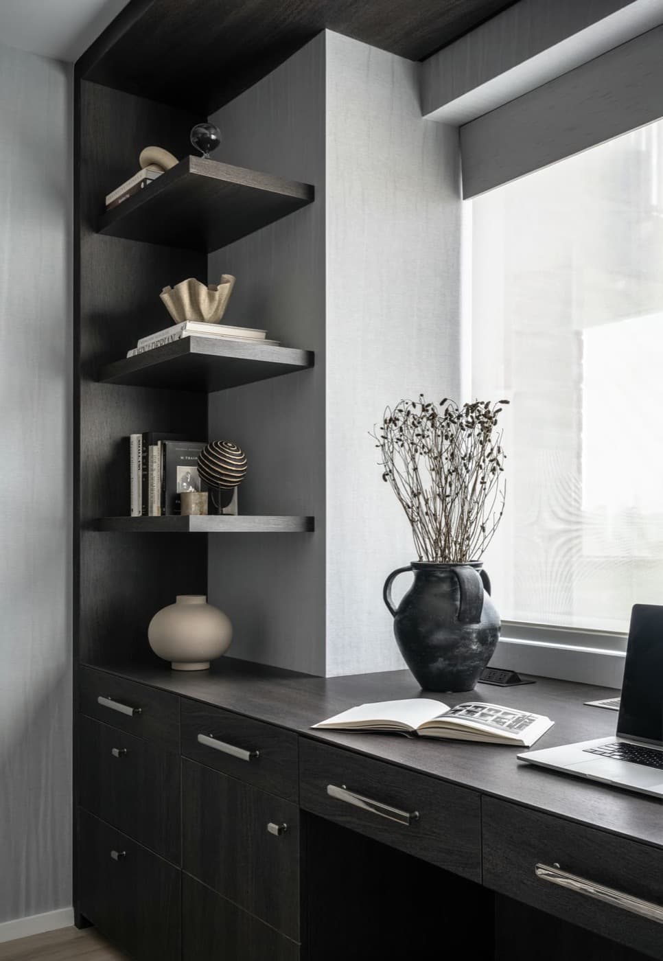 Study featuring built-in dark timber desk with floating corner shelves beside a large window