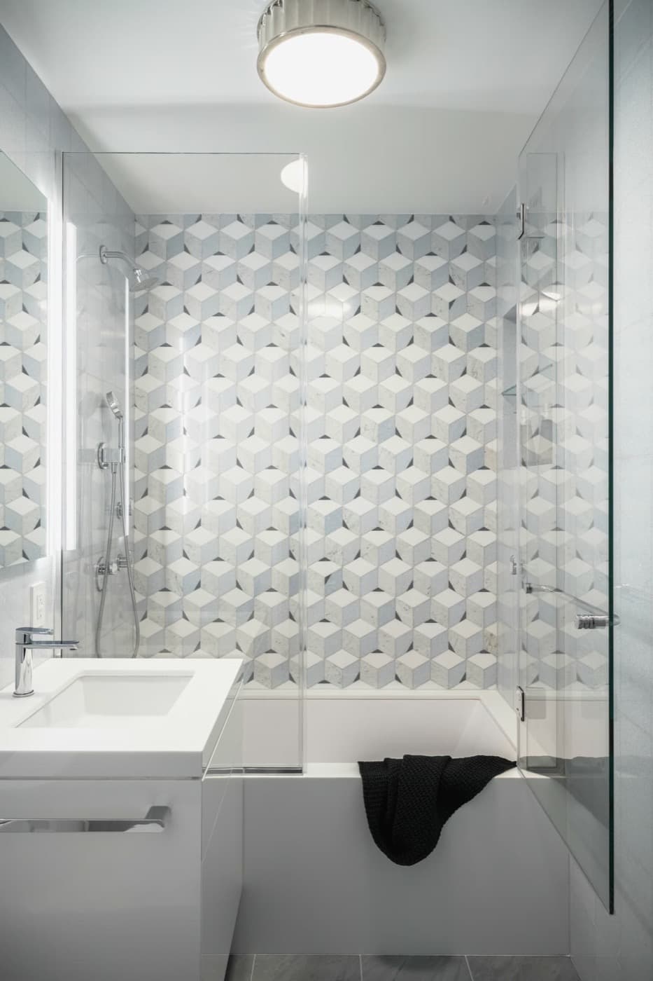 Bathroom with geometric patterned tile accent wall above a glass-enclosed bathtub and white vanity