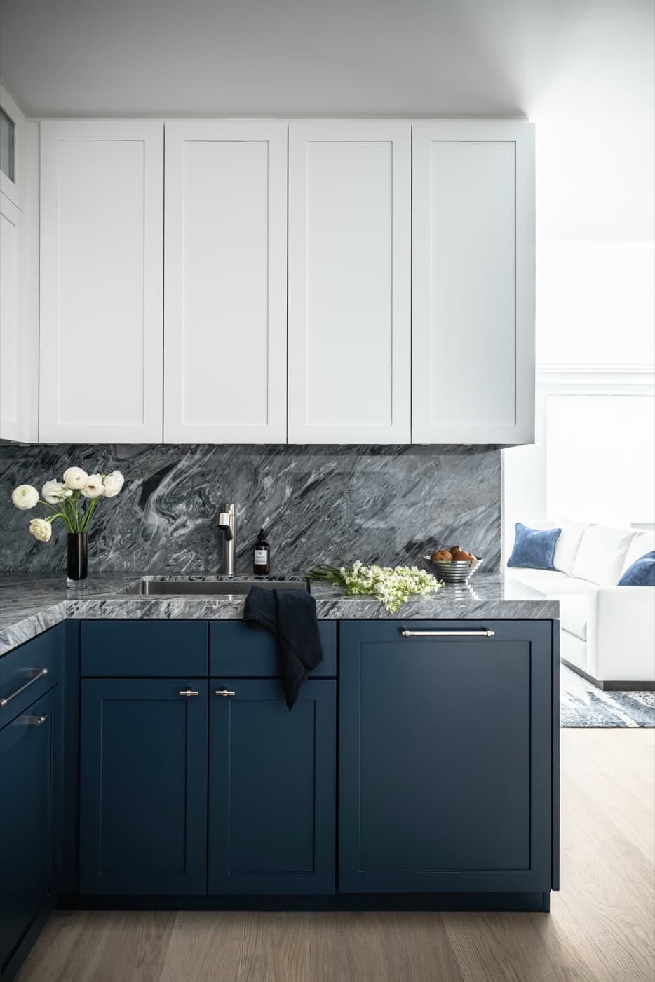 Kitchen with white upper cabinetry, dark blue lower cabinets, and figured grey stone surfaces