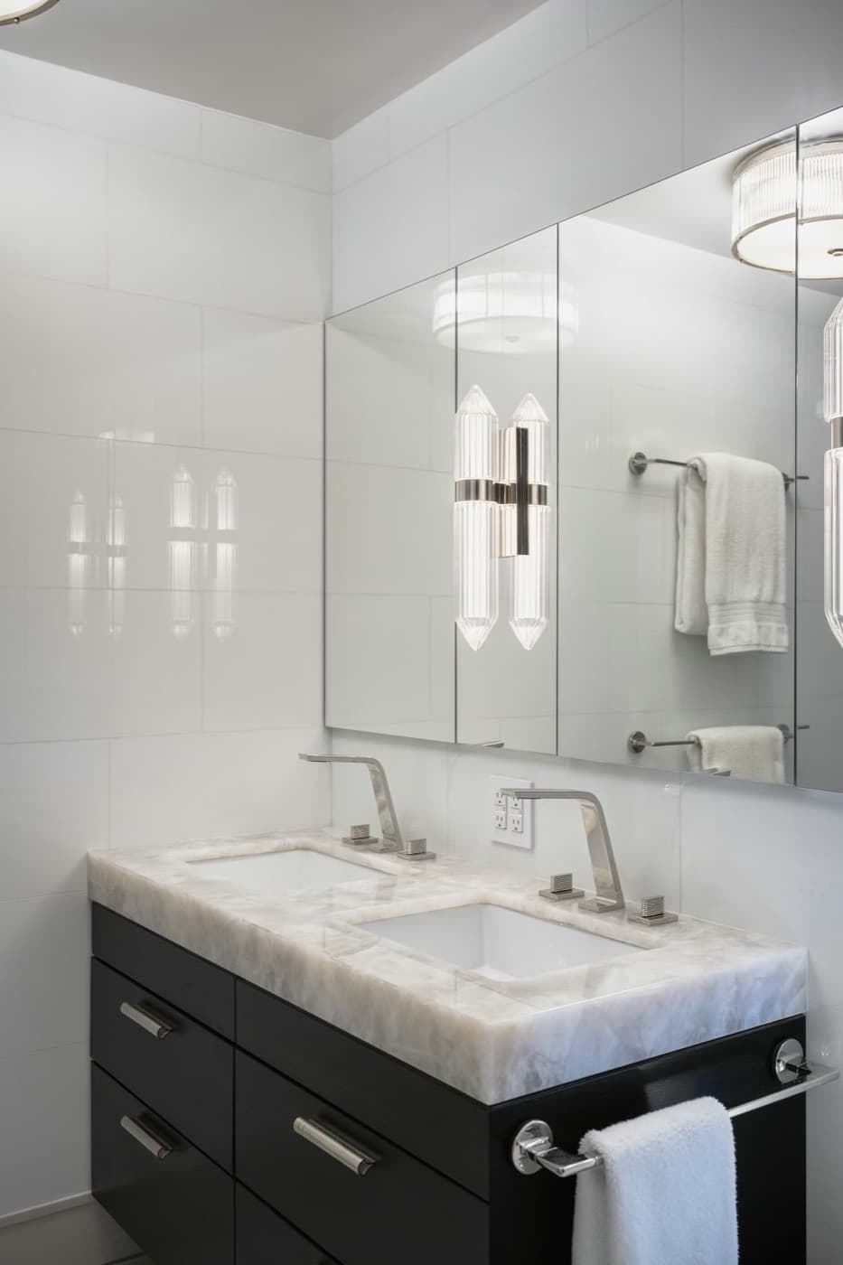 Bathroom featuring dark double vanity with thick pale stone countertop and mirrored medicine cabinets