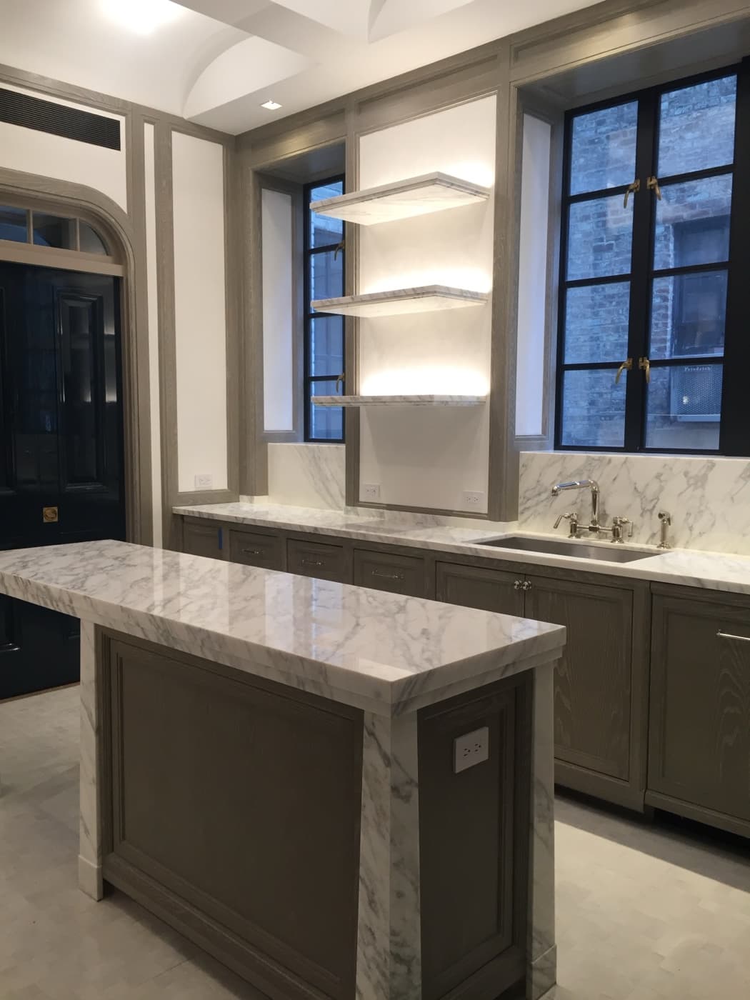 Kitchen with pale veined stone island, custom wood cabinetry, and illuminated floating shelves