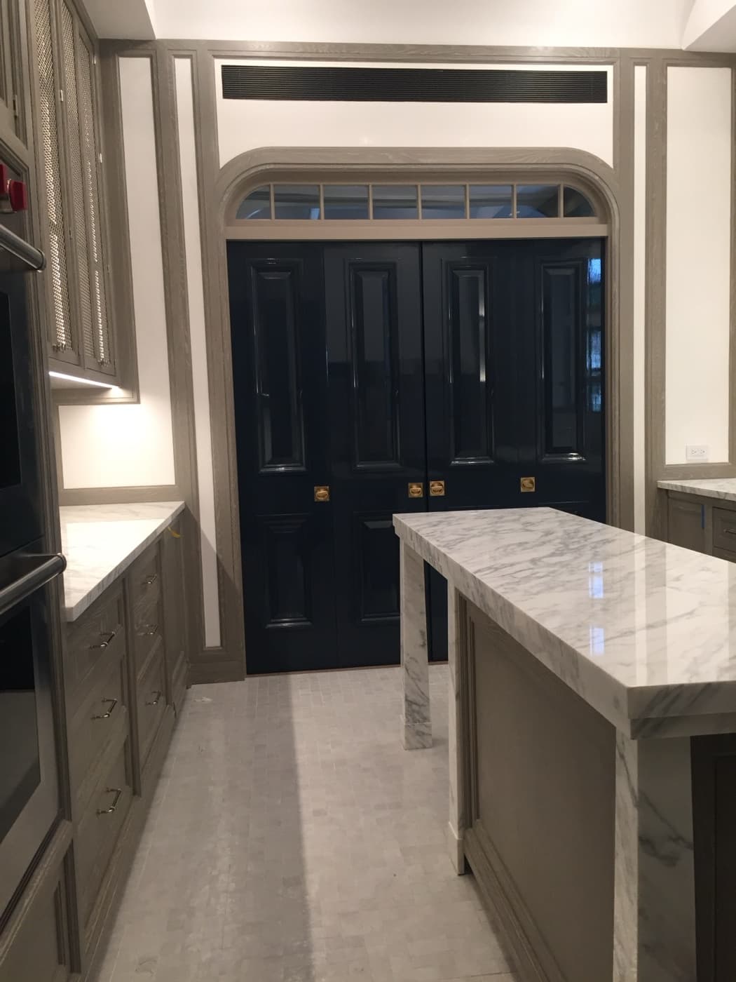 Kitchen featuring a pale veined stone island, custom cabinetry, and glossy dark panelled doors