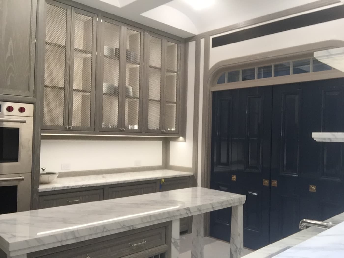 Kitchen with grey-toned timber mesh cabinetry, pale veined stone island, and dark double doors